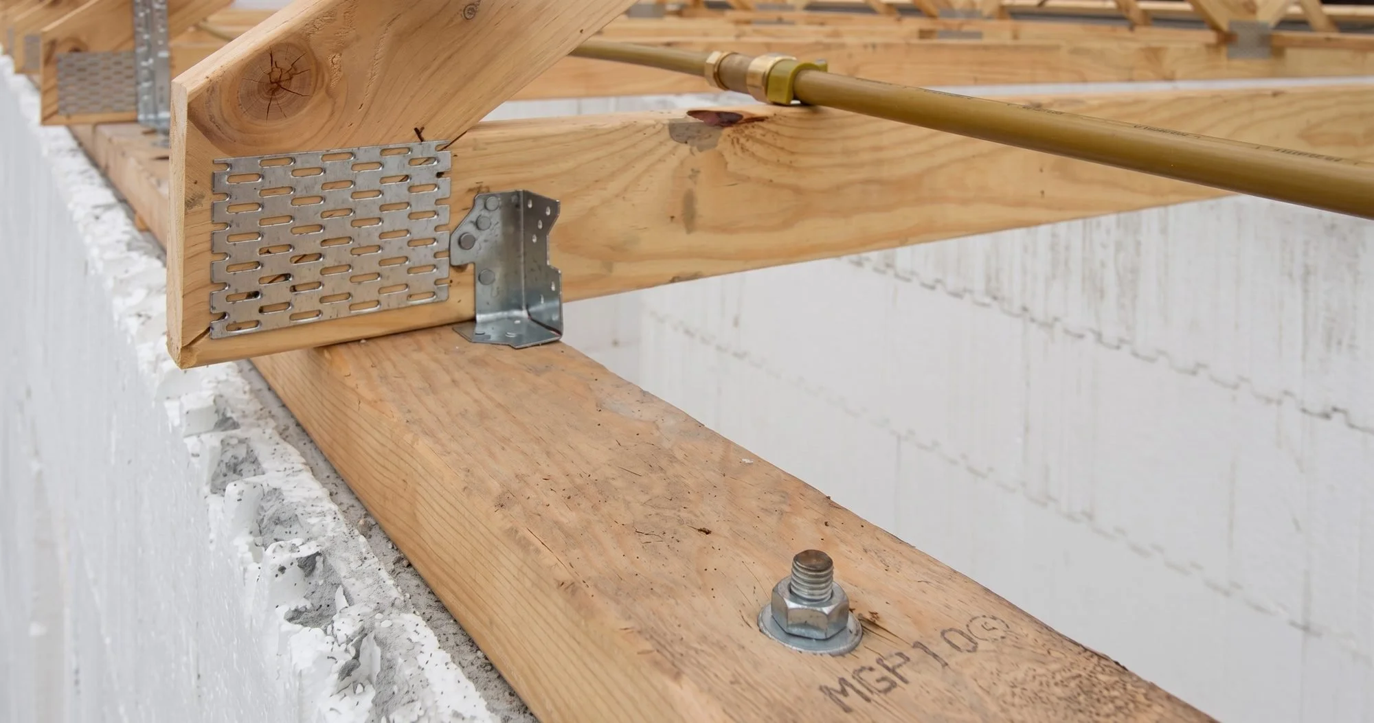 Close-up of wooden beams and metal brackets on a construction site, with a brass pipe attached to the beams.