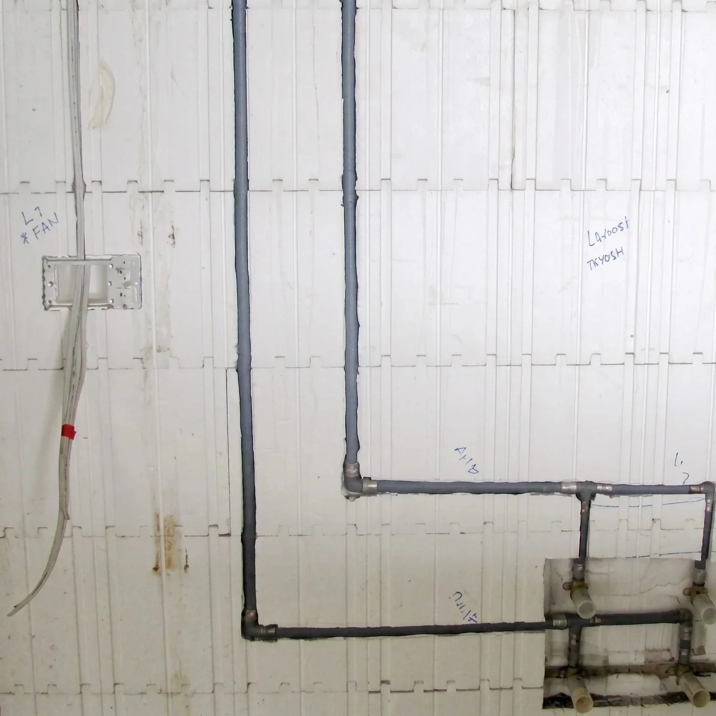 Pipes and electrical wiring installed on a white wall, with some handwritten notes and labels nearby.