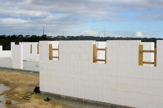 Construction site with white concrete block walls and wooden supports, under a cloudy sky.