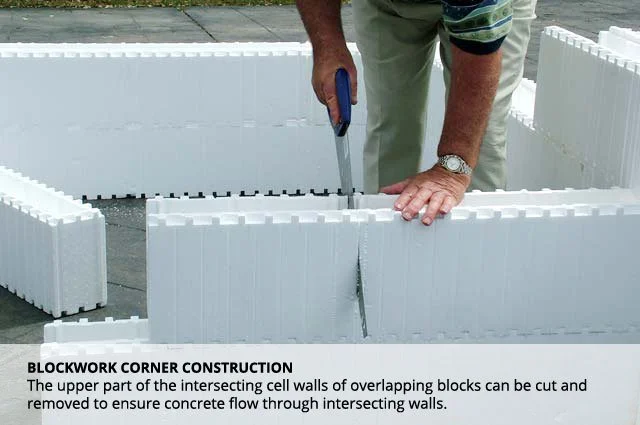 A person using a handsaw to cut an intersecting foam block wall for blockwork corner construction, with additional foam blocks nearby.