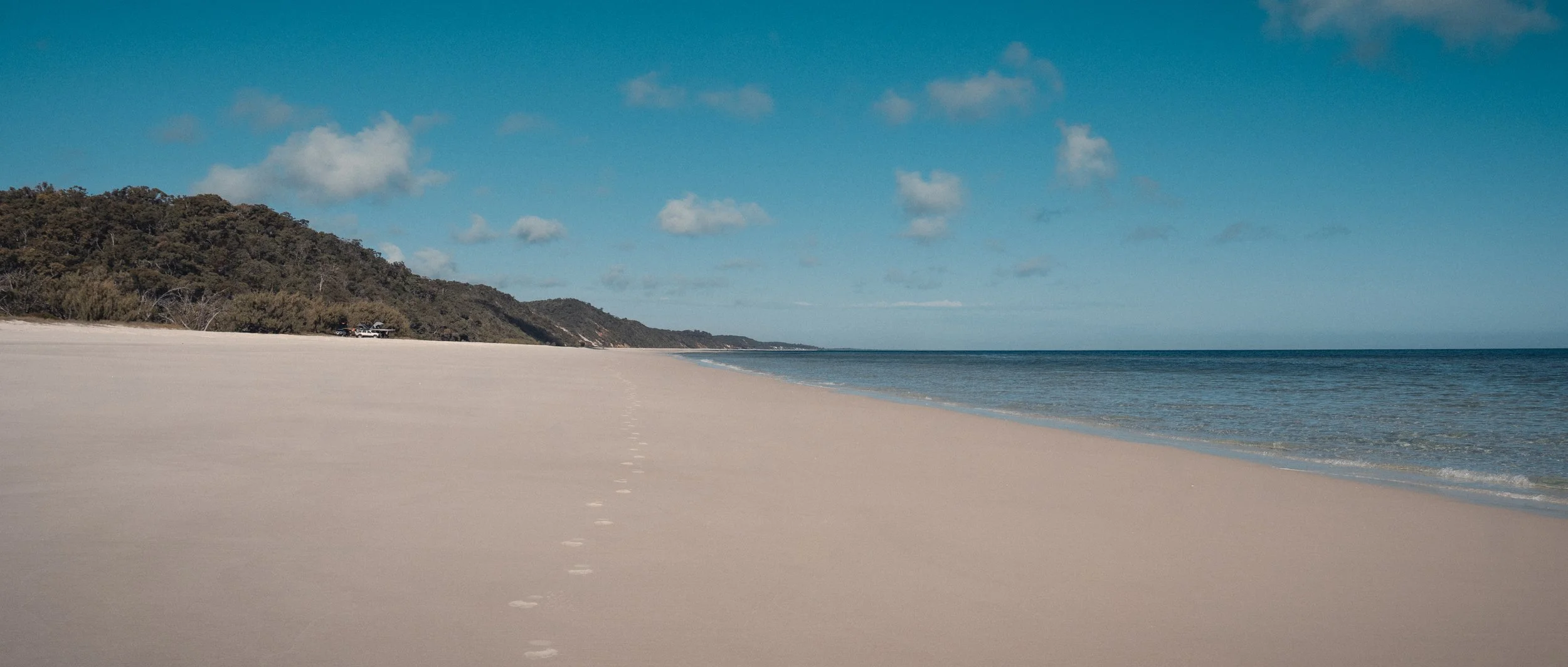 Quiet sandy shoreline beside pale blue water and open sky.
