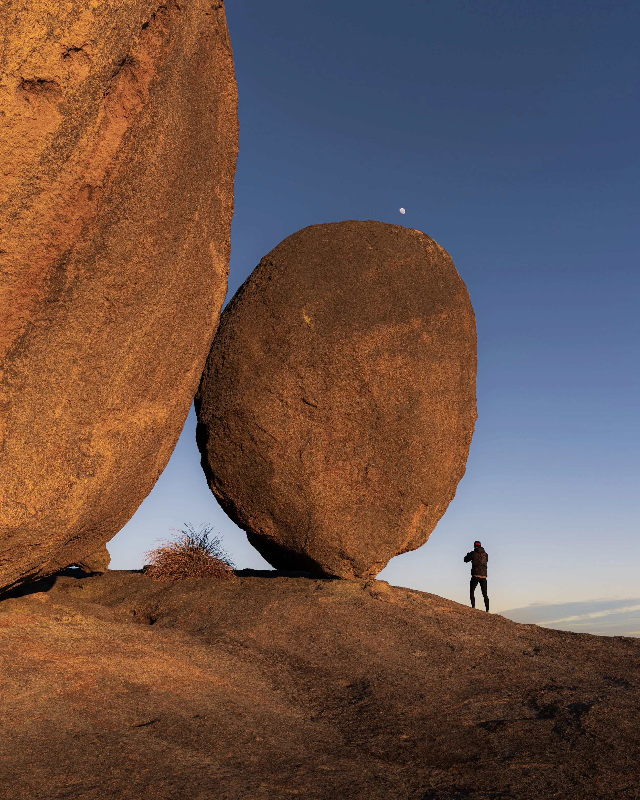 Natural red-rock arch rising above a small human figure under a clear blue sky.
