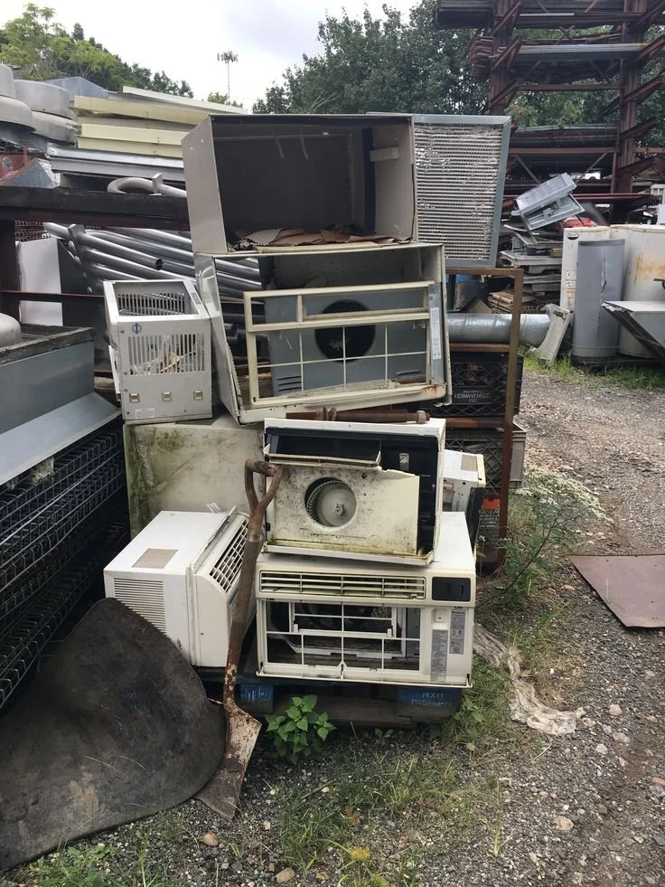 Four household appliances on curb: refrigerator, stove, washing machine, dryer in neighborhood with brick house and trees.