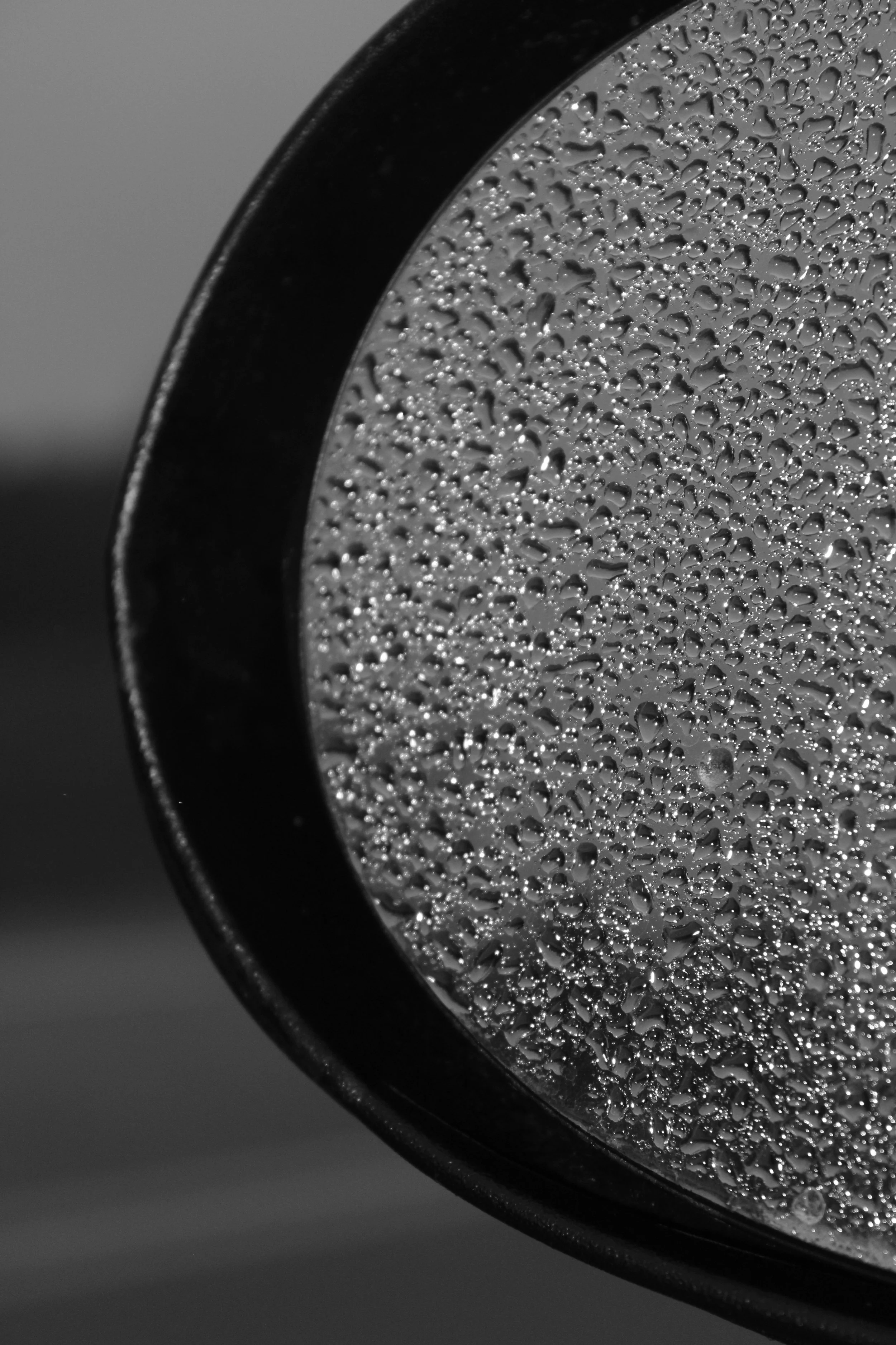 Close-up of a side view mirror with water droplets on its reflective surface, partially visible against a gray background.