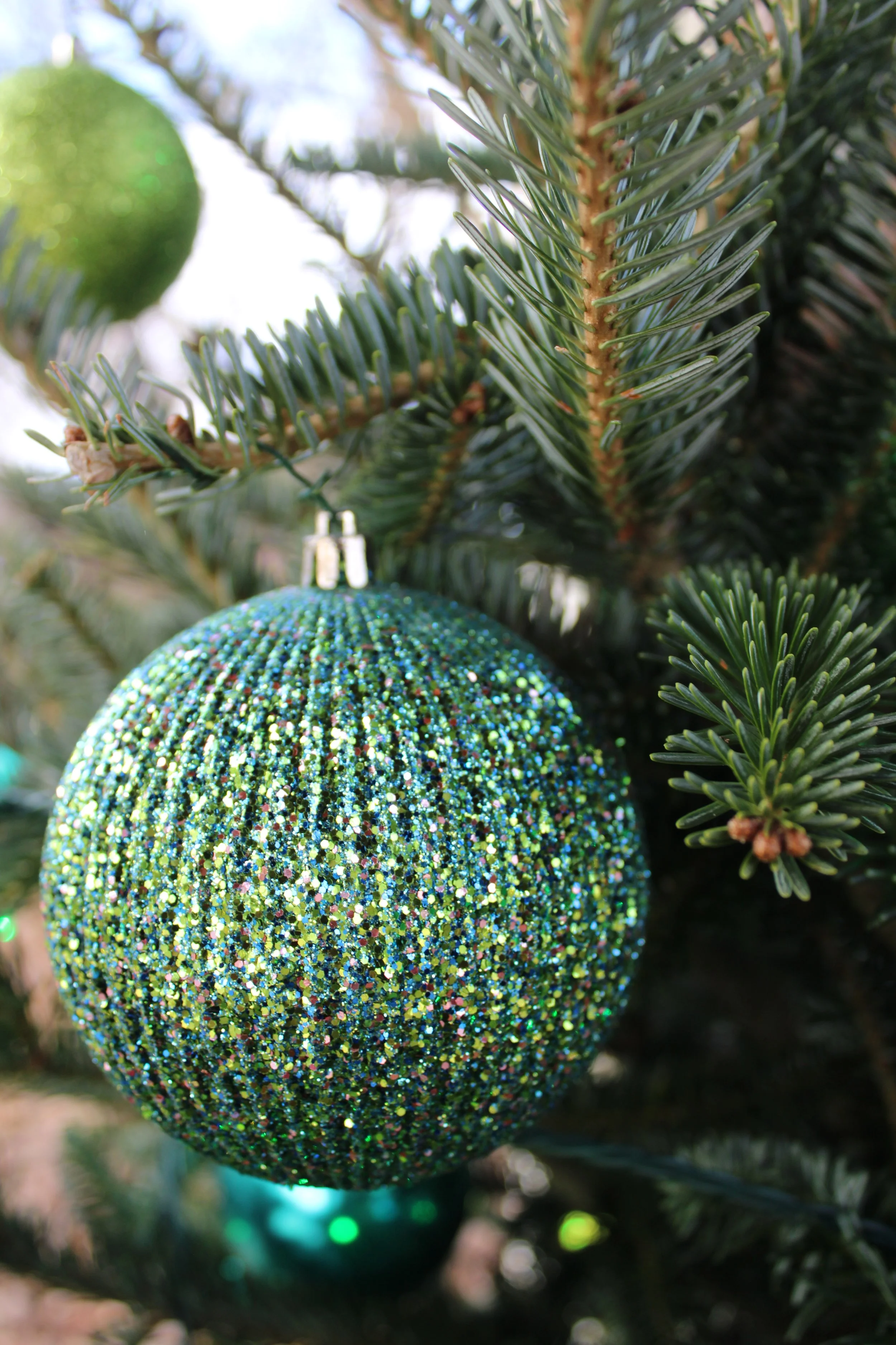 A close-up of a Christmas tree branch with a glittery, multicolored ornament hanging from it.