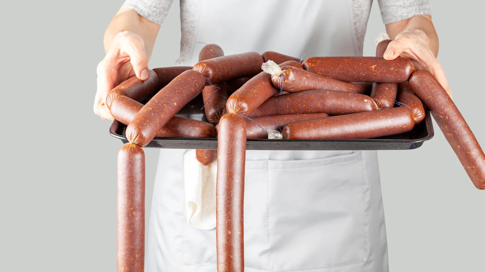 An image of someone in a butchers apron, holding a tray of sausages representing a content sausage factory