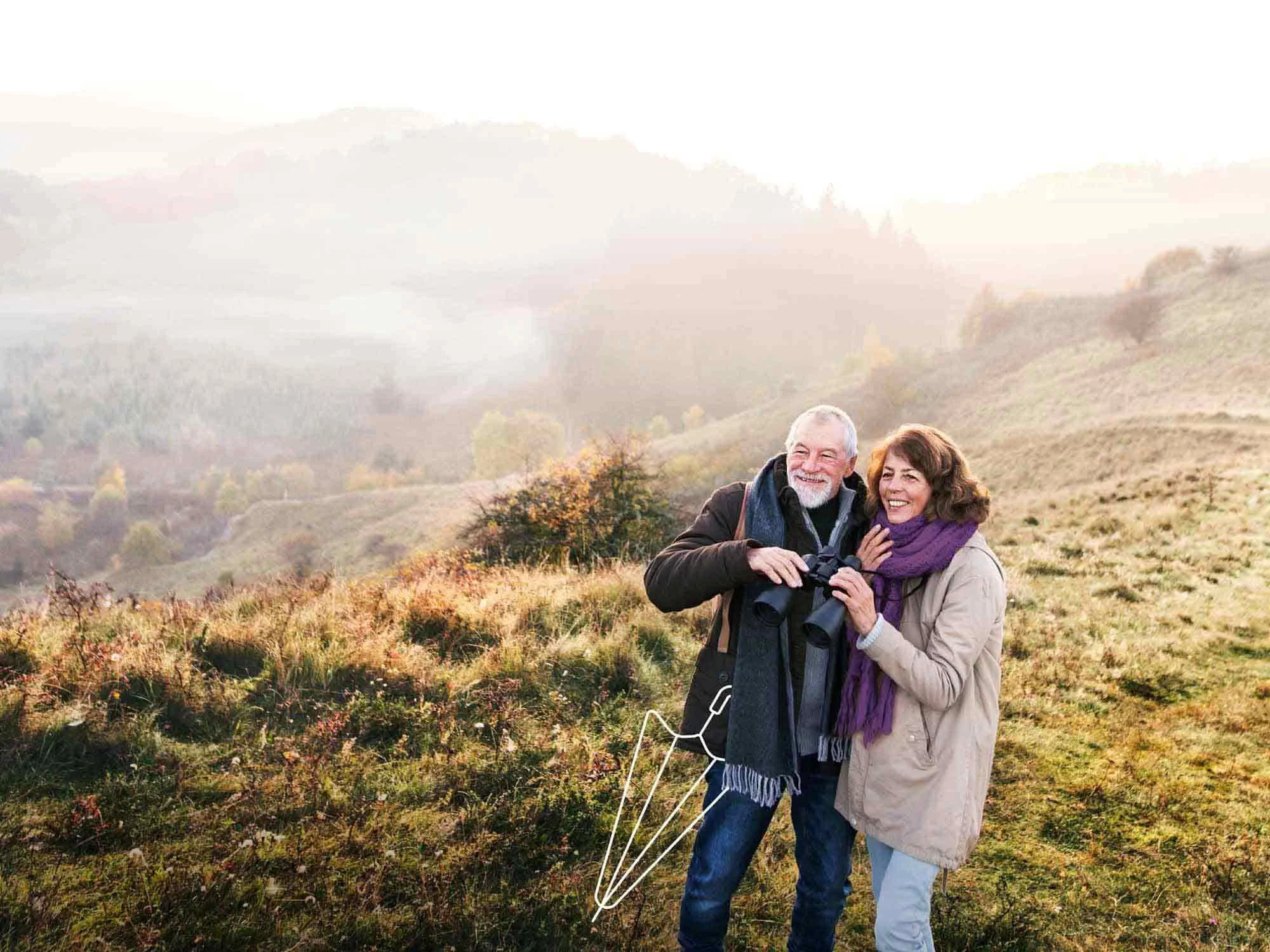 A couple enjoying retirement on a hike. They are holding binoculars and an illustrated umbrella is at their feet
