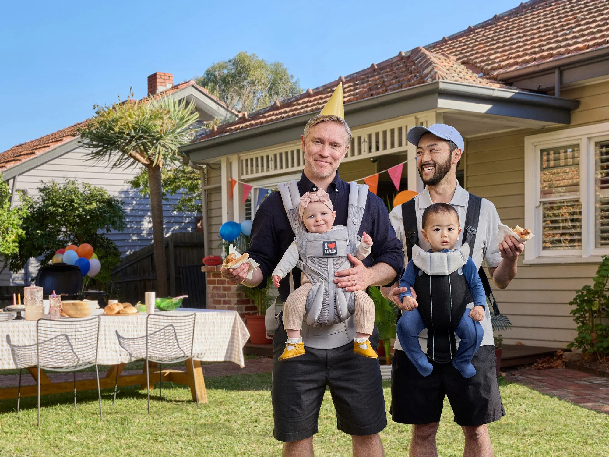 Two dads holding babies at BBQ