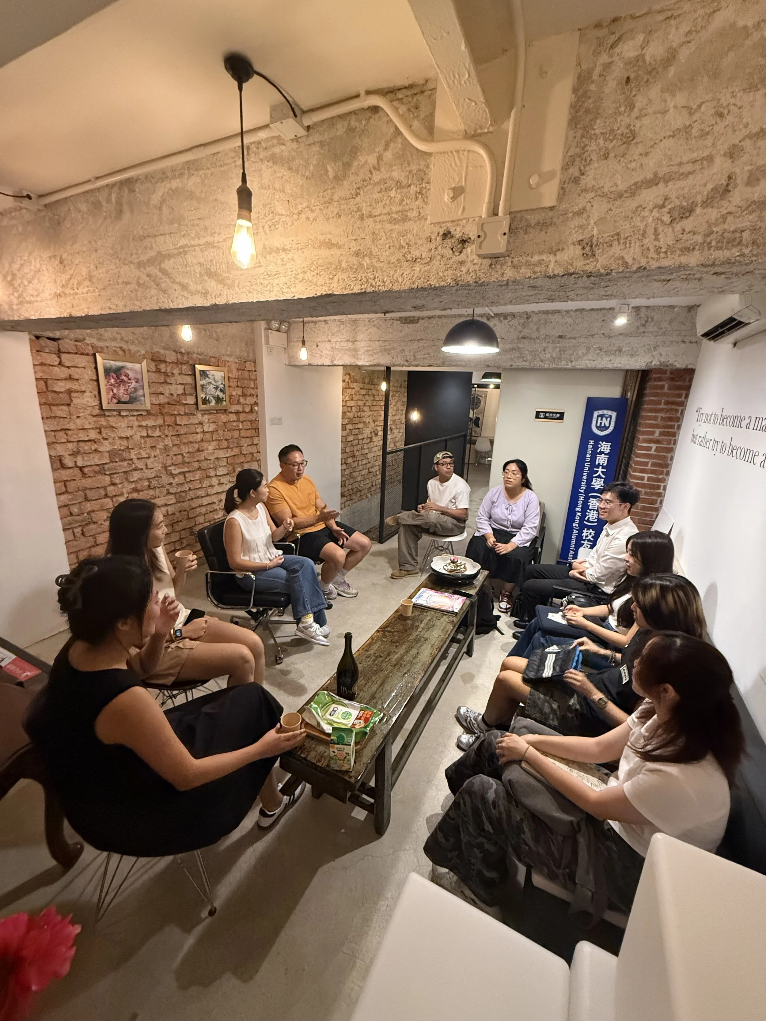 A group of people sitting in a circle in a cozy room with brick walls and warm lighting, engaged in conversation.