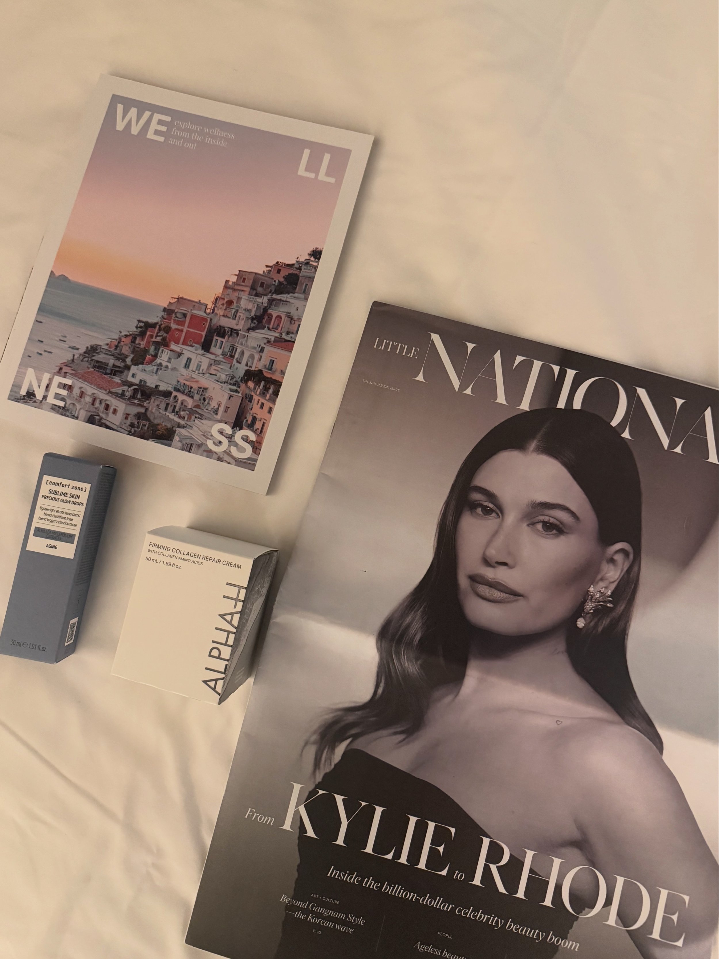 A magazine titled 'Kylie Rhoades' with a woman on the cover, and a poster with a coastal town and sunset in the background, along with beauty products. hayley bieber clean girl