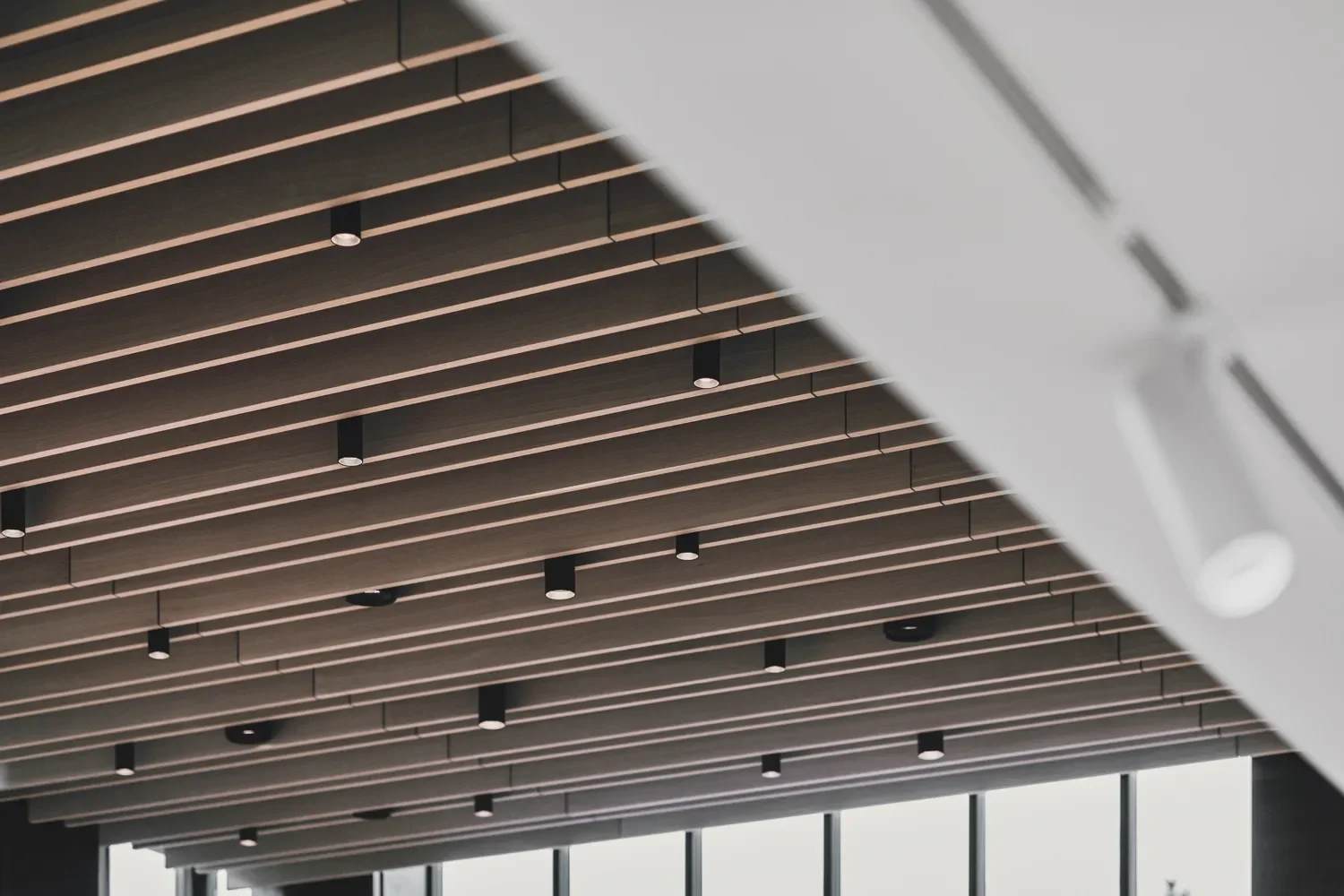 Interior ceiling with wooden slats and small ceiling lights by LIK Lighting, part of a modern building interior in the Teddy Bear Museum, Denmark, with large window panels.
