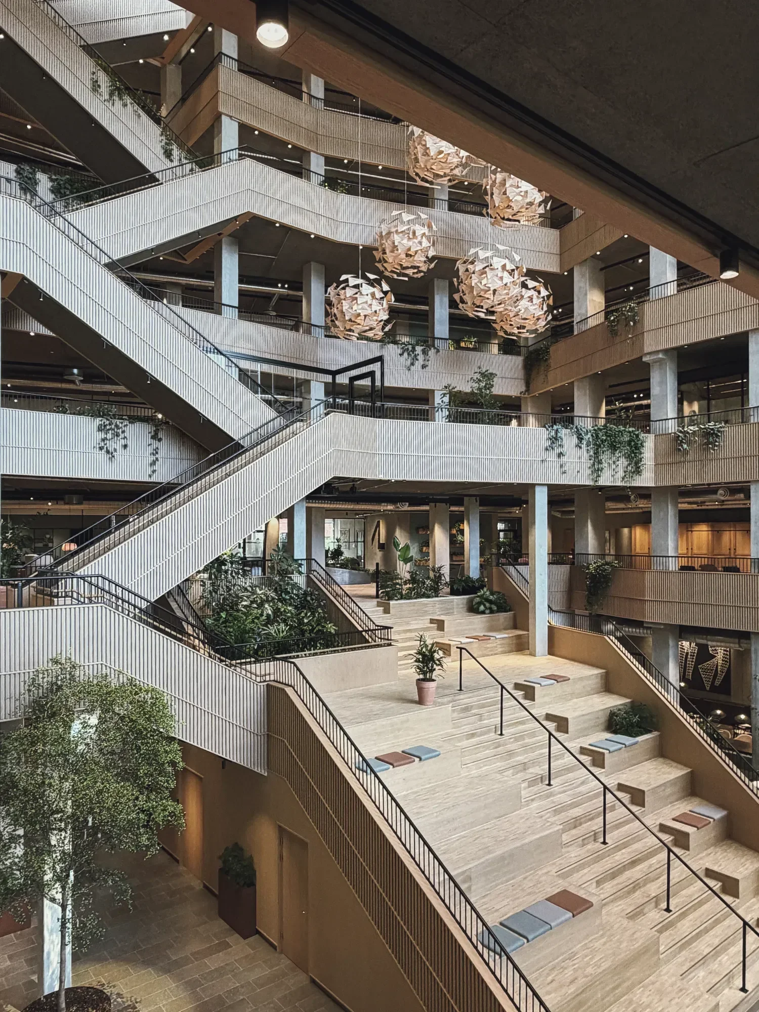 Interior view of a multi-story office building for Arbejdernes Landsbank with open spaces, featuring stairs, railings, hanging light fixtures by LIK Lighting, and plants.