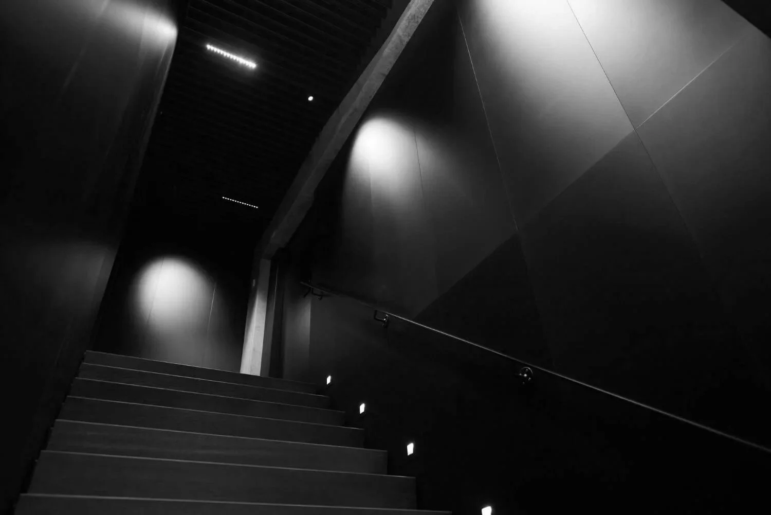 Dark interior staircase with small embedded lights along the side walls, leading upward, with minimalistic design and muted lighting.