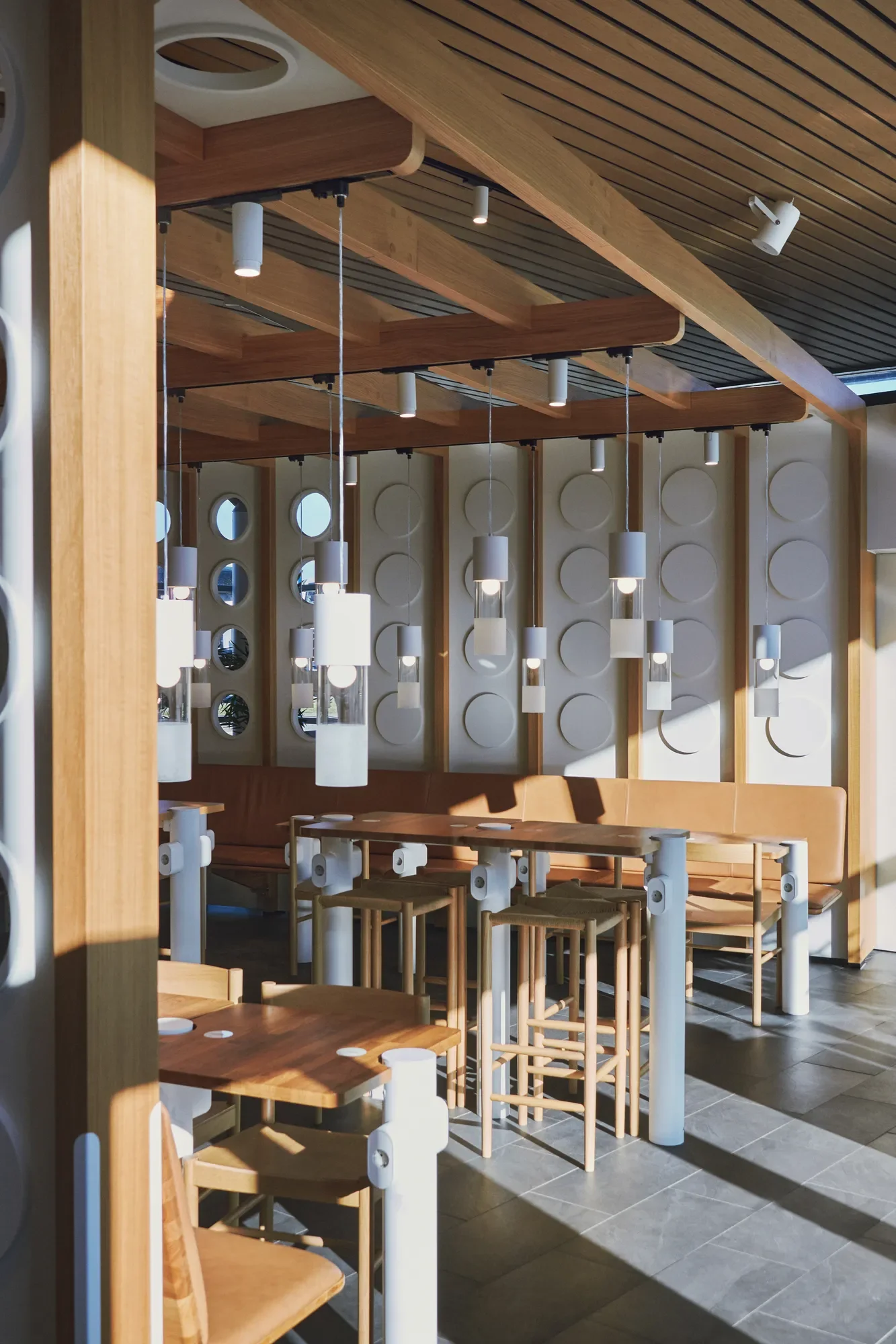Modern restaurant dining area with wood tables, bar-height seating, pendant lights, and decorative circular wall panels with lighting design by LIK Lighting