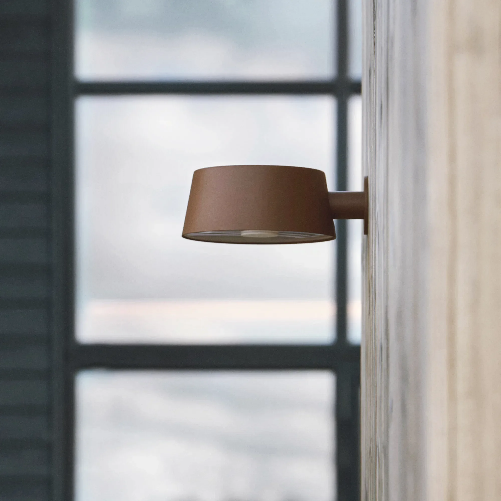 Close-up of an outdoor light fixture by LIK Lighting, a window and a wooden wall.
