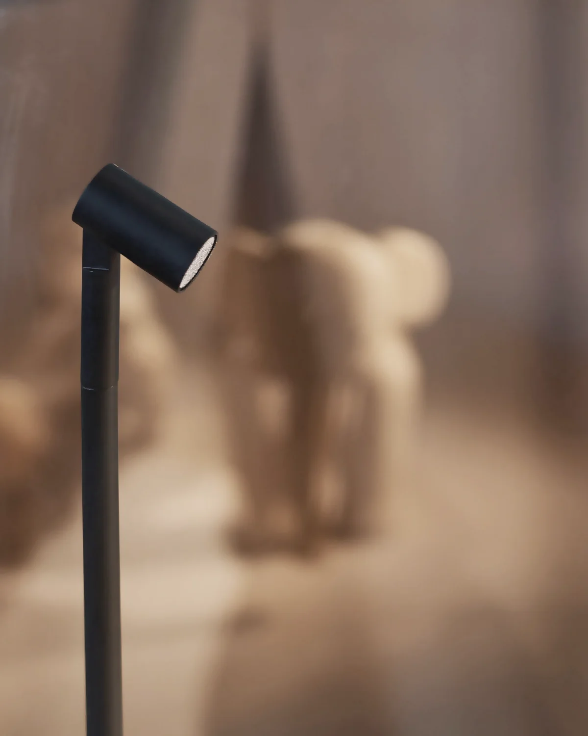 Minimalist black cylindrical floor lamp - Dispaly Lighting - casting a soft shadow on a warm beige wall.