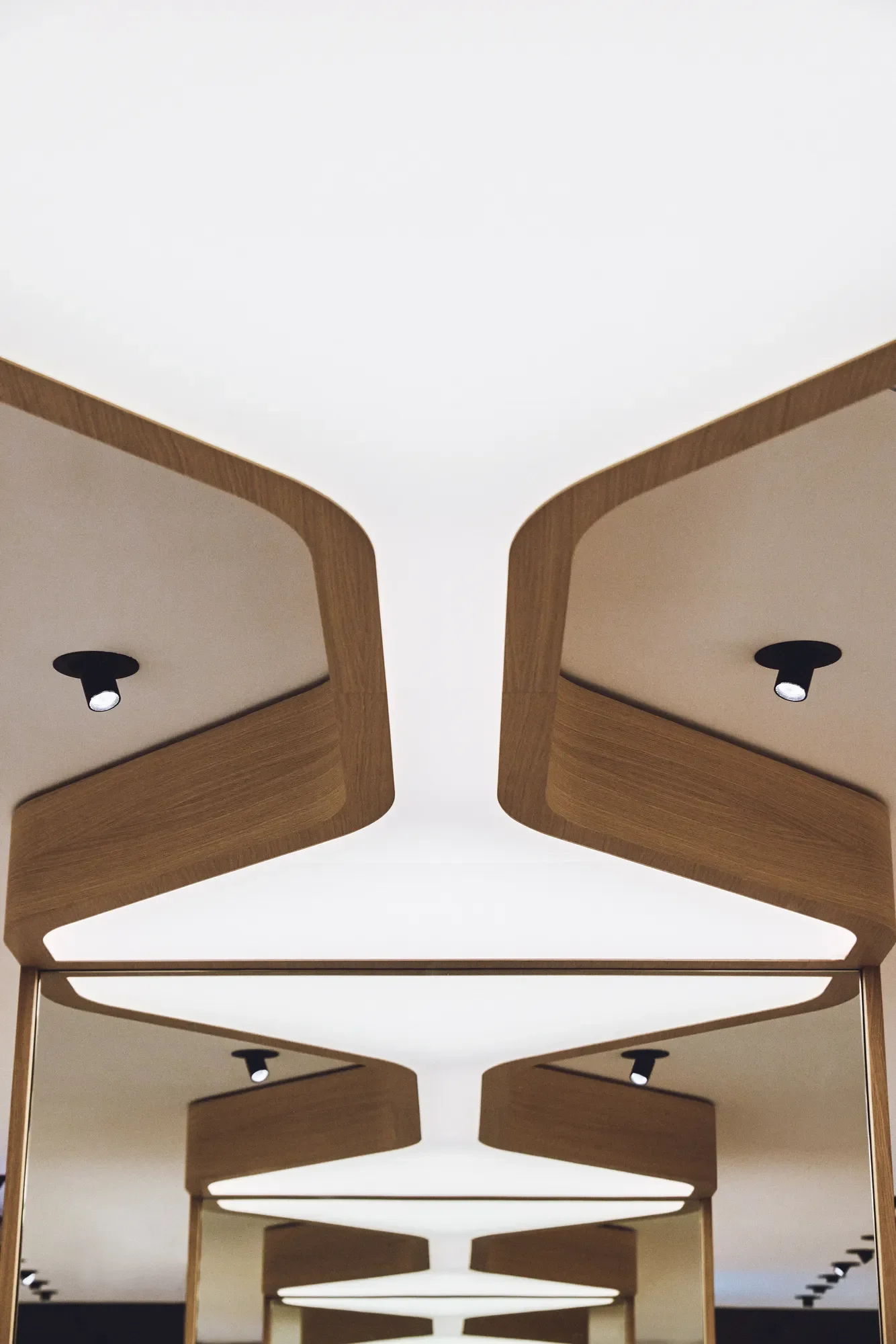 Ceiling with wooden panel accents and multiple recessed spotlights, reflected in a mirrored surface by LIK Lighting.