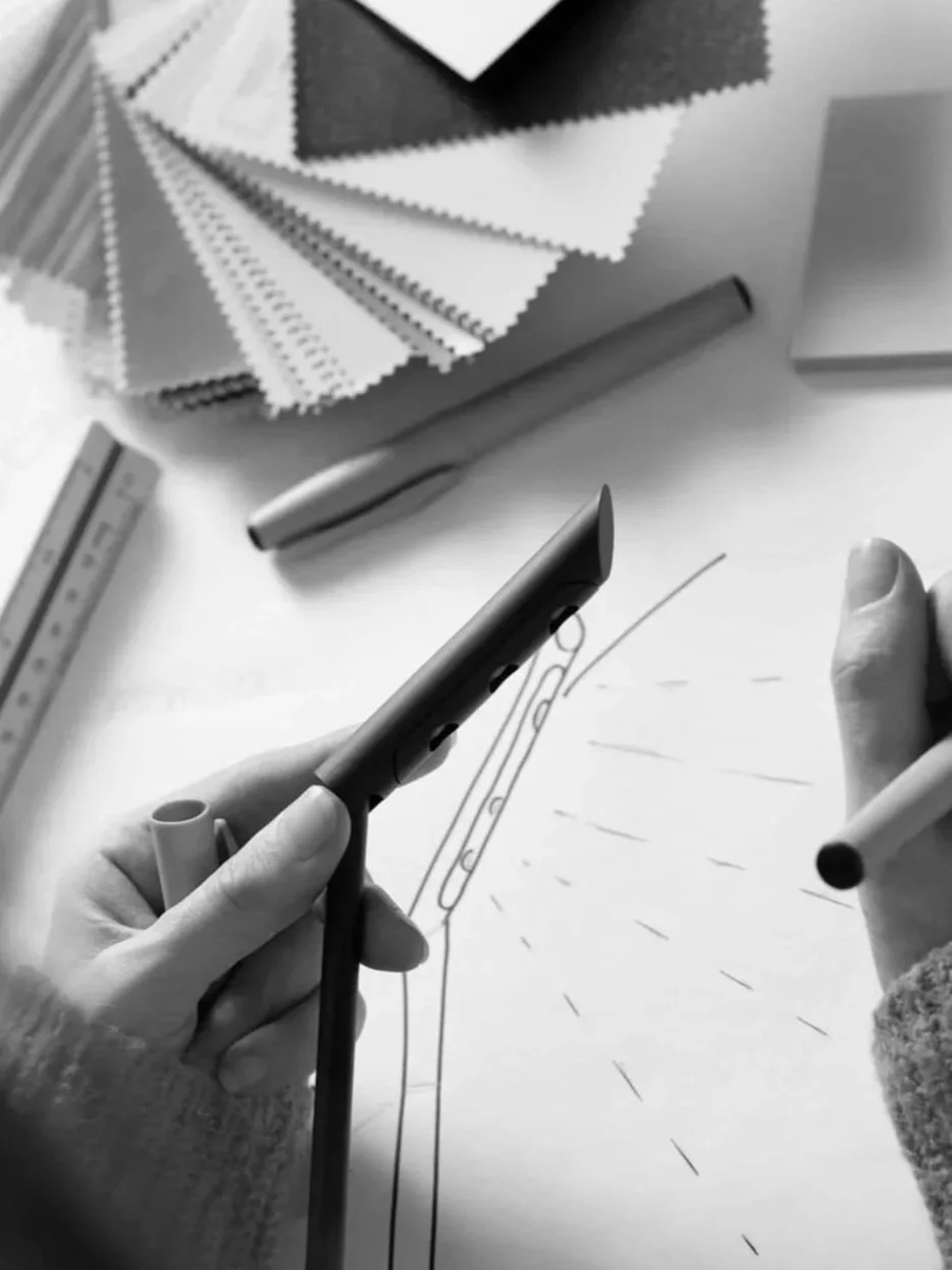 A LIK Lighting expert drawing a technical diagram of an open pocket knife on paper with colored pencil, surrounded by markers, color samples, and a ruler.