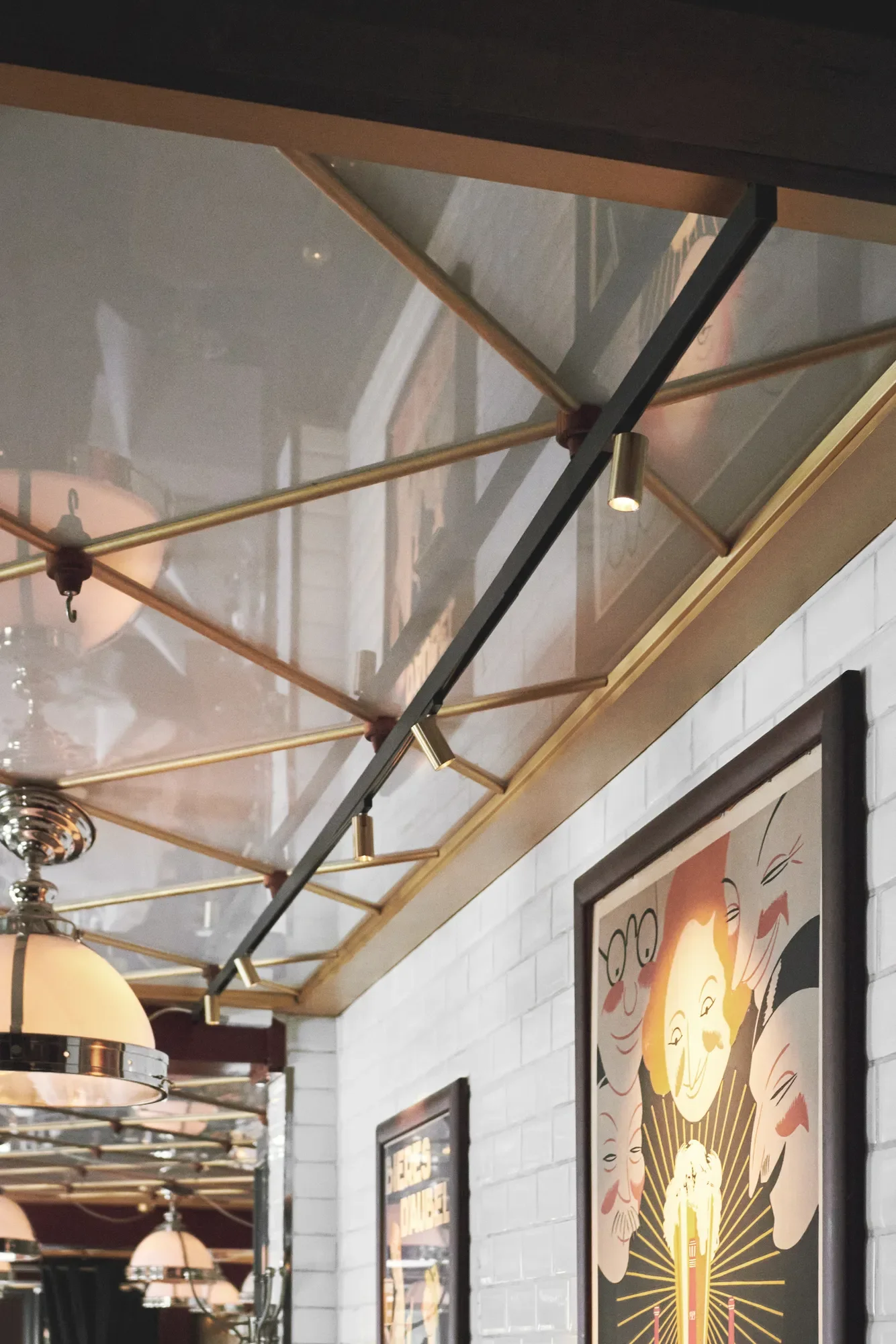 Interior of Café Victor in Copenhagen with a decorative ceiling mirror, framed art posters on white brick walls, and spotlights by LIK Lighting.