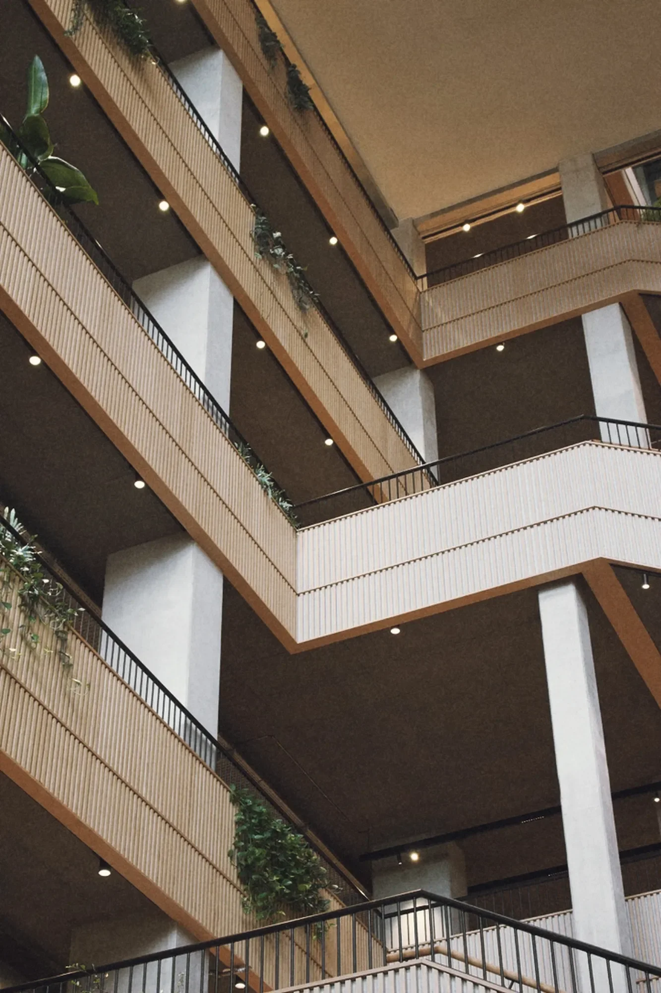 Multiple floors of Arbejdernes Landsbank, a modern building with wooden railings, plants, and ceiling lights by LiK Lighting.