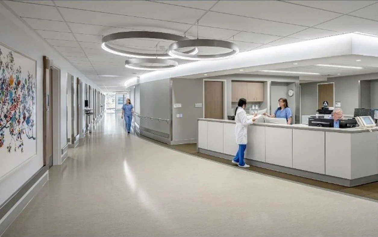 Hospital reception area with staff and nurses engaging in work, modern decor, and bright lighting.
