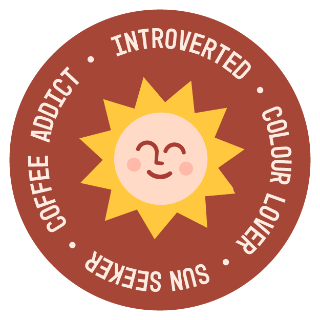 A circular badge with a smiling sun in the center, surrounded by a brown border with white text that reads: 'COFFEE ADDICT', 'INTROVERTED', 'COLOUR LOVER', and 'SUN SEEKER'.