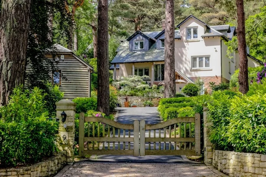 A scenic view of a large house surrounded by trees and greenery, with a stone and wooden gate at the front entrance.