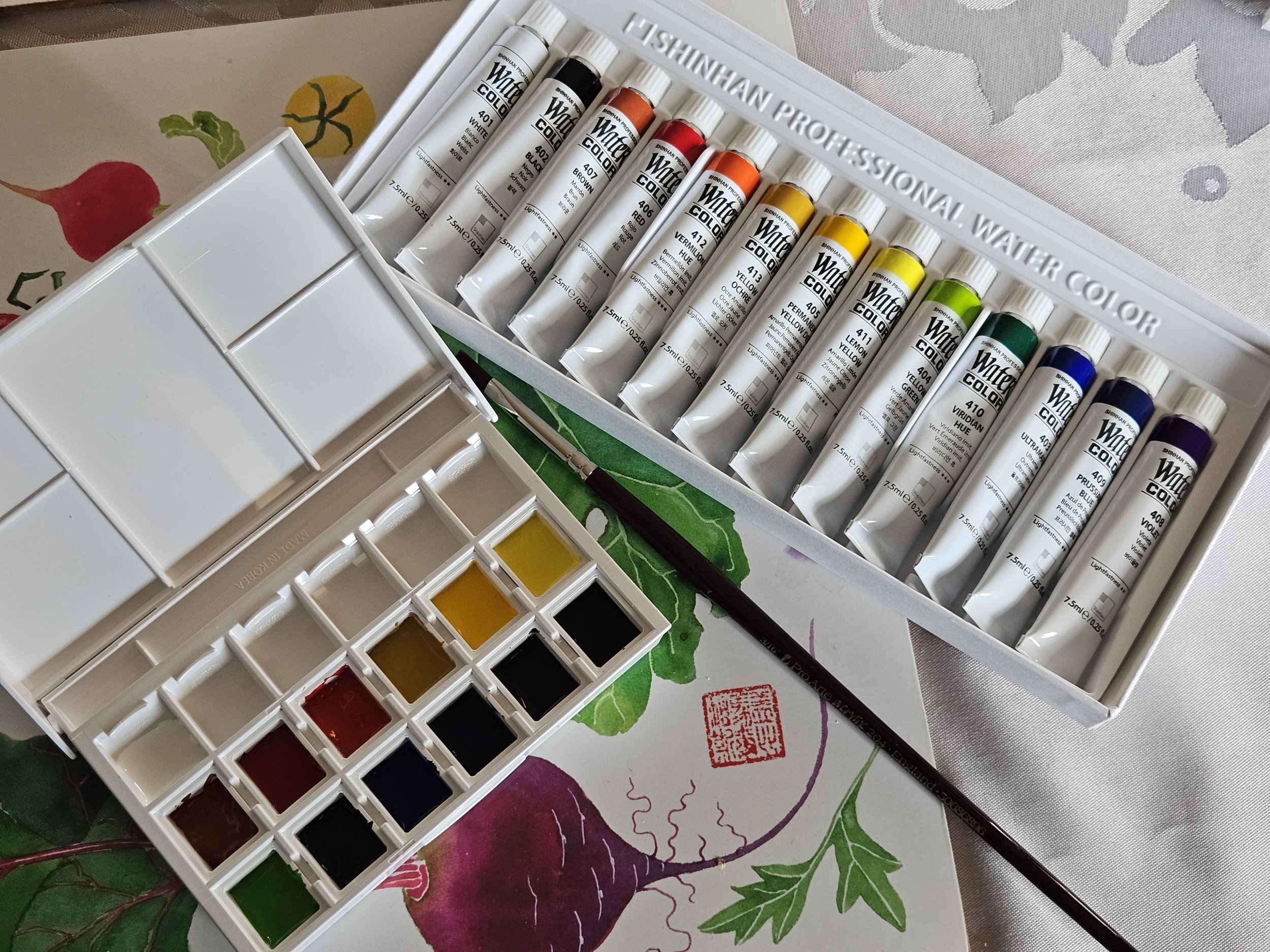 A set of watercolor paints in tubes and a palette of mixed paints on a surface with a floral design.