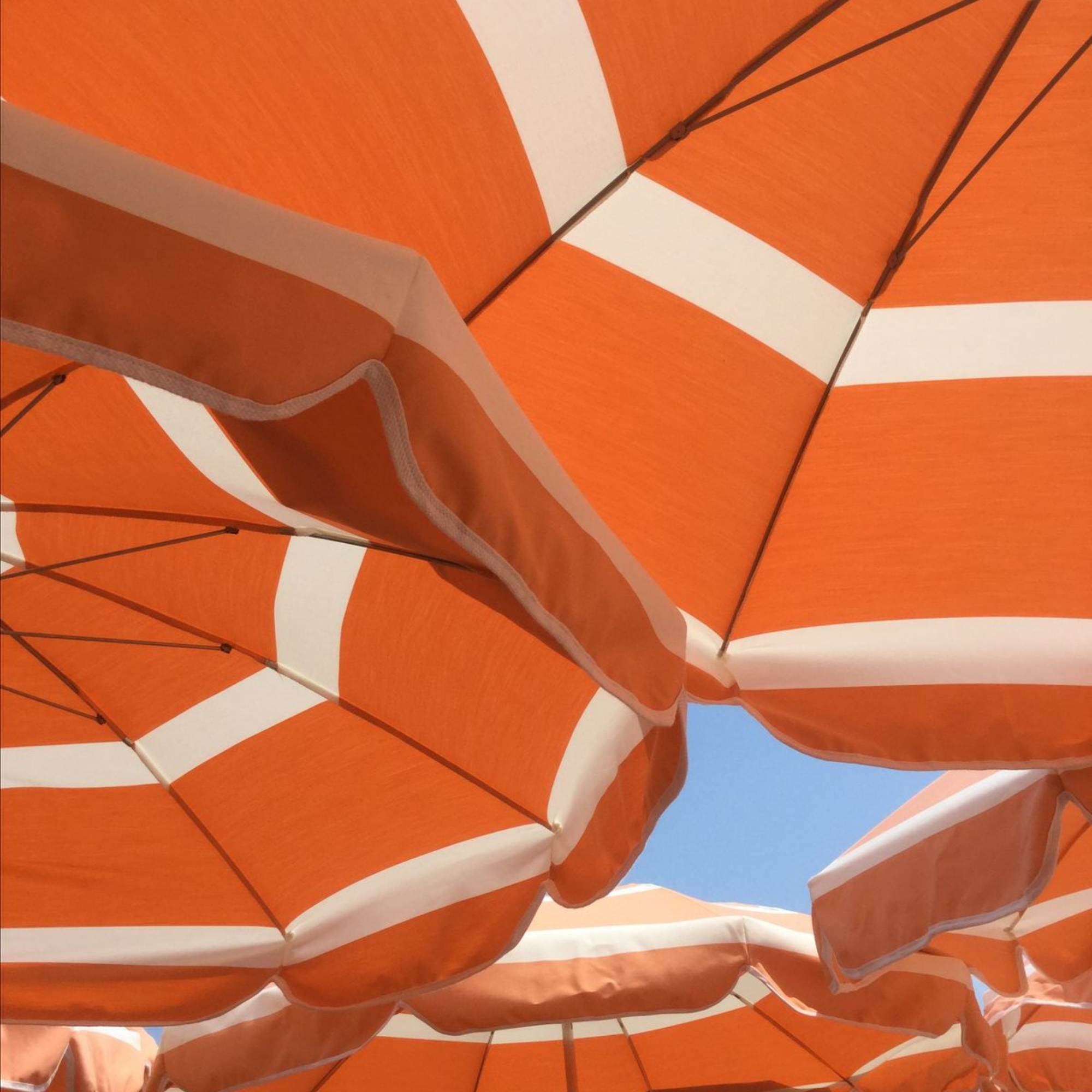 Multiple orange and white striped beach umbrellas viewed from below against a blue sky.