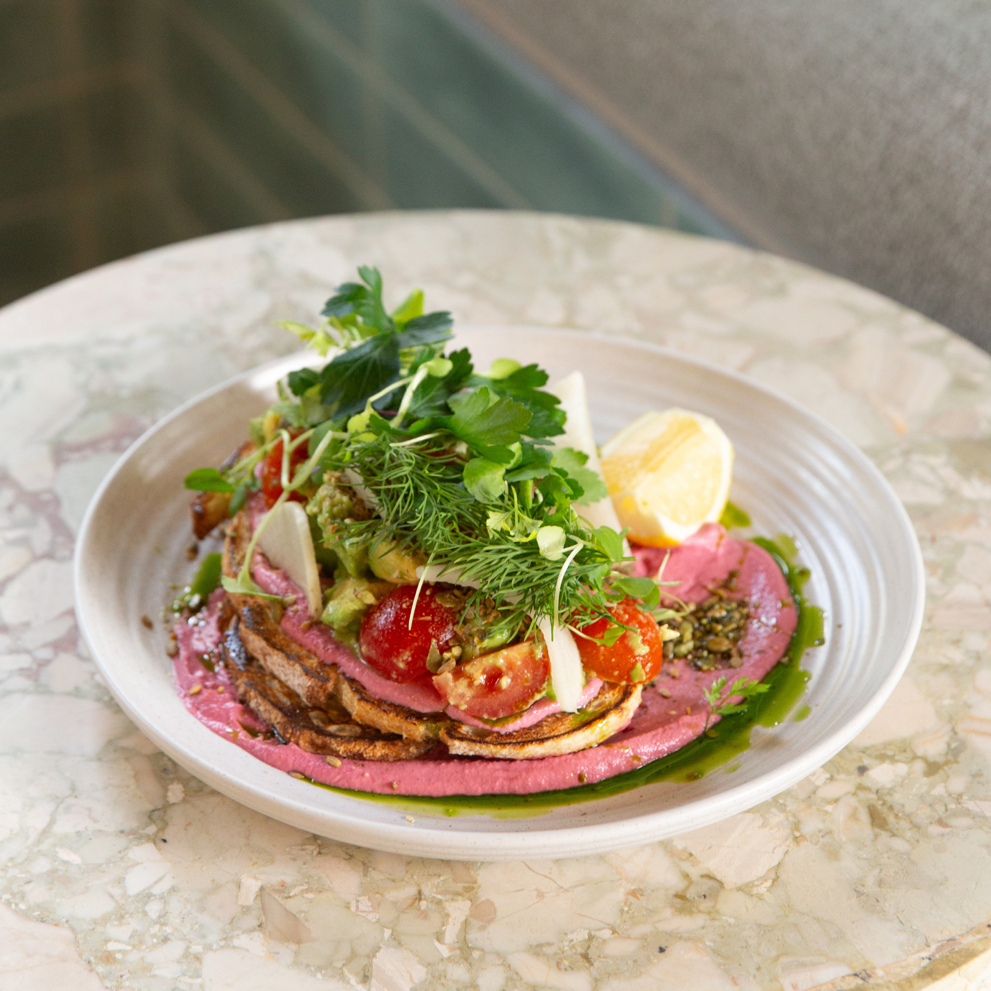 A dish with layered ingredients including sliced tomatoes, greens, and possibly cheese, garnished with fresh herbs on a marble surface.