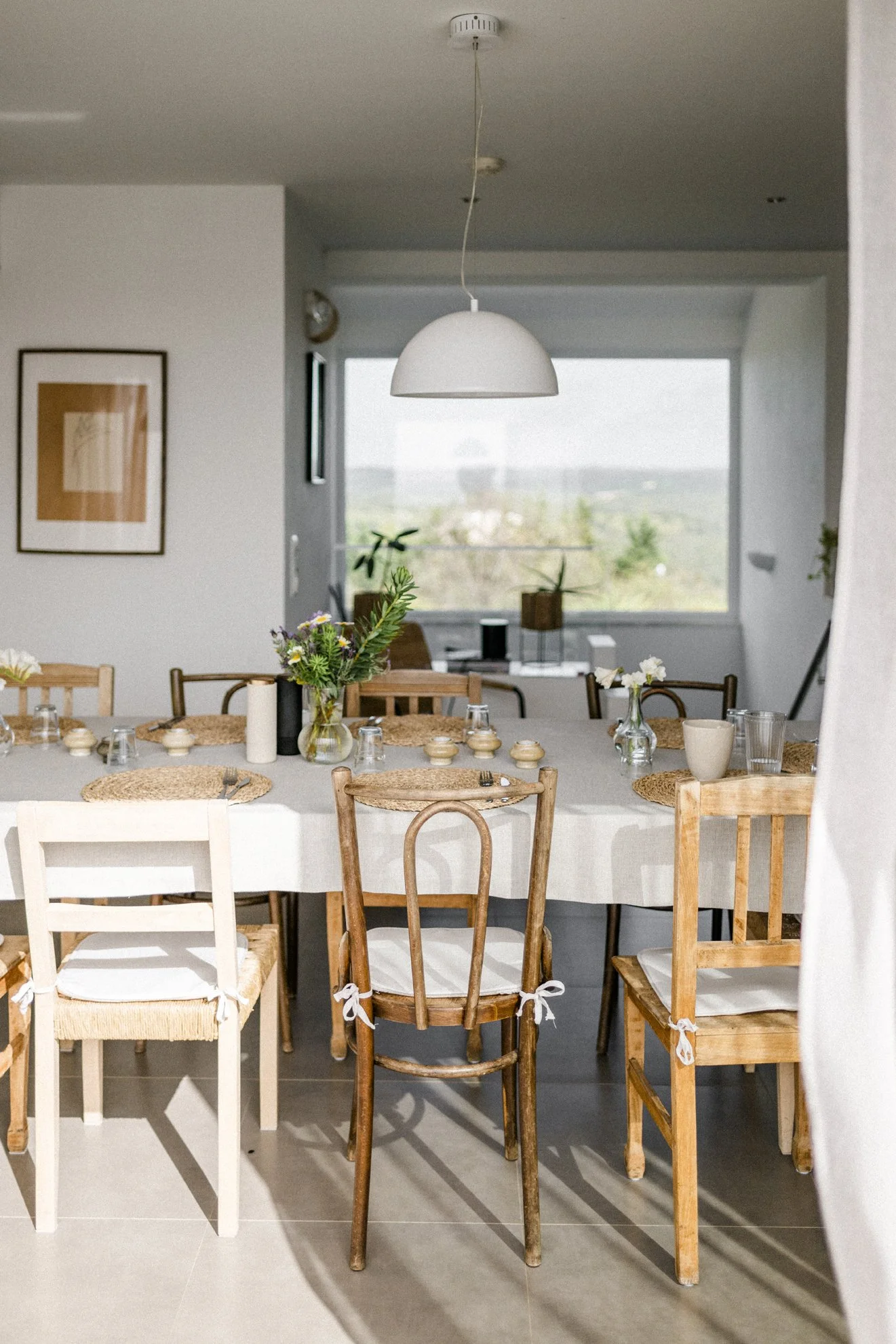 Ein Esstisch mit mehreren Stühlen, Dekorationsgegenständen und einem Blumenstrauß in einer modernen, hellen Wohnung.