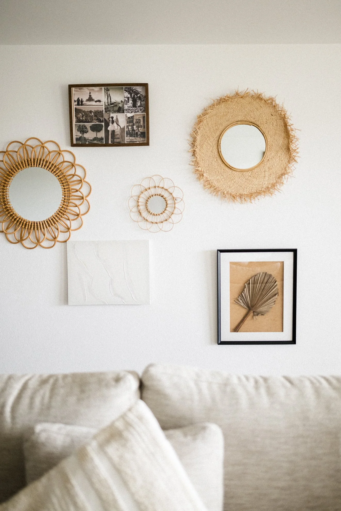 Wohnzimmerwand mit dekorativen Pflanzen, Spiegel und Fotocollage, beige Couch im Vordergrund