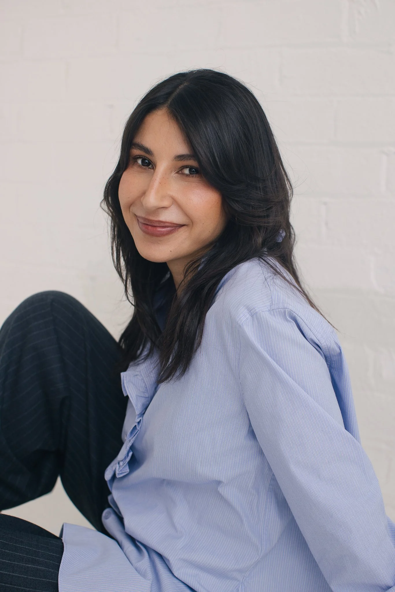 Portrait of Denise Osman, the author, smilin, seated with a lean on white backdrop