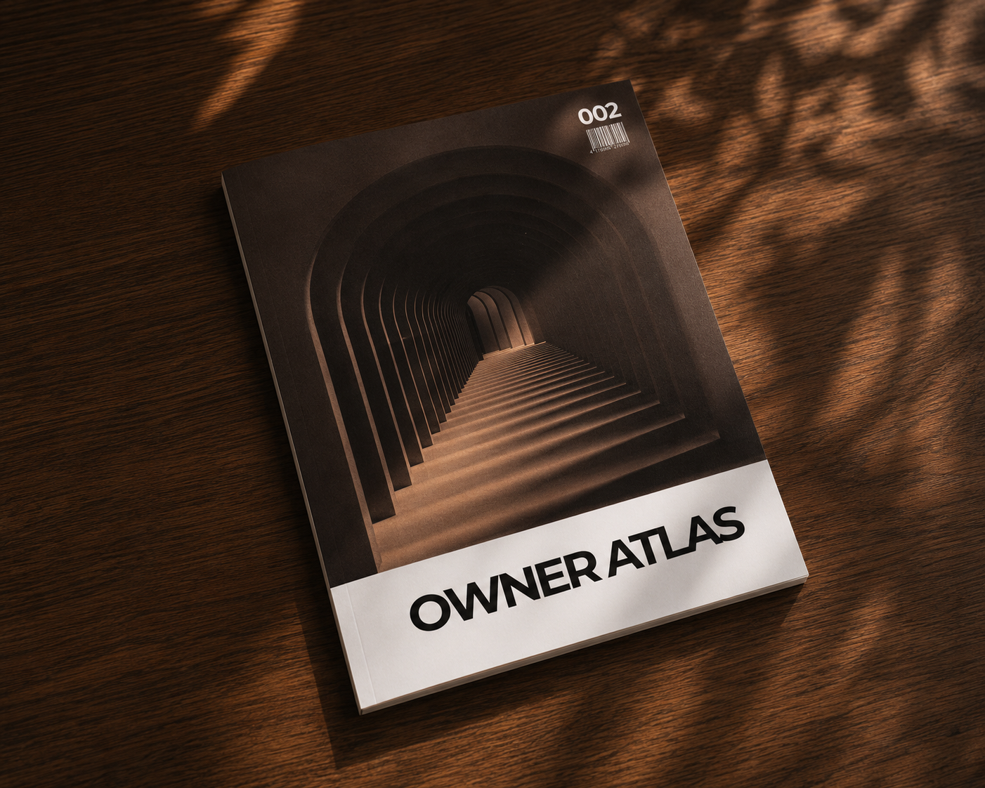 Ein Magazin mit einem Cover, das ein Bild eines dunklen, tunnelartigen Flurs mit wiederholenden arched Linien zeigt. Der Titel lautet "OWNER ATLAS" und die Ausgabe ist Nummer 002.