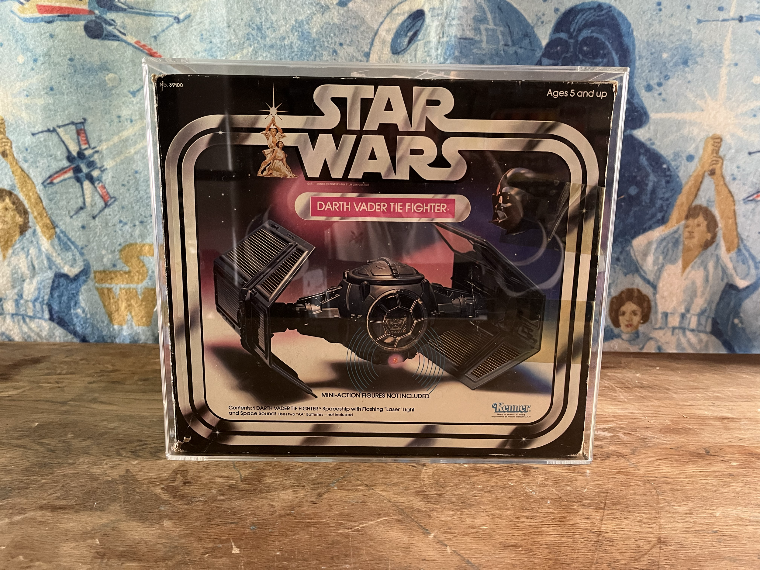 Back of a Star Wars toy packaging box featuring Darth Vader and a TIE fighter with flashing laser light and sound effect, set against a background of a space scene with stars and planets.