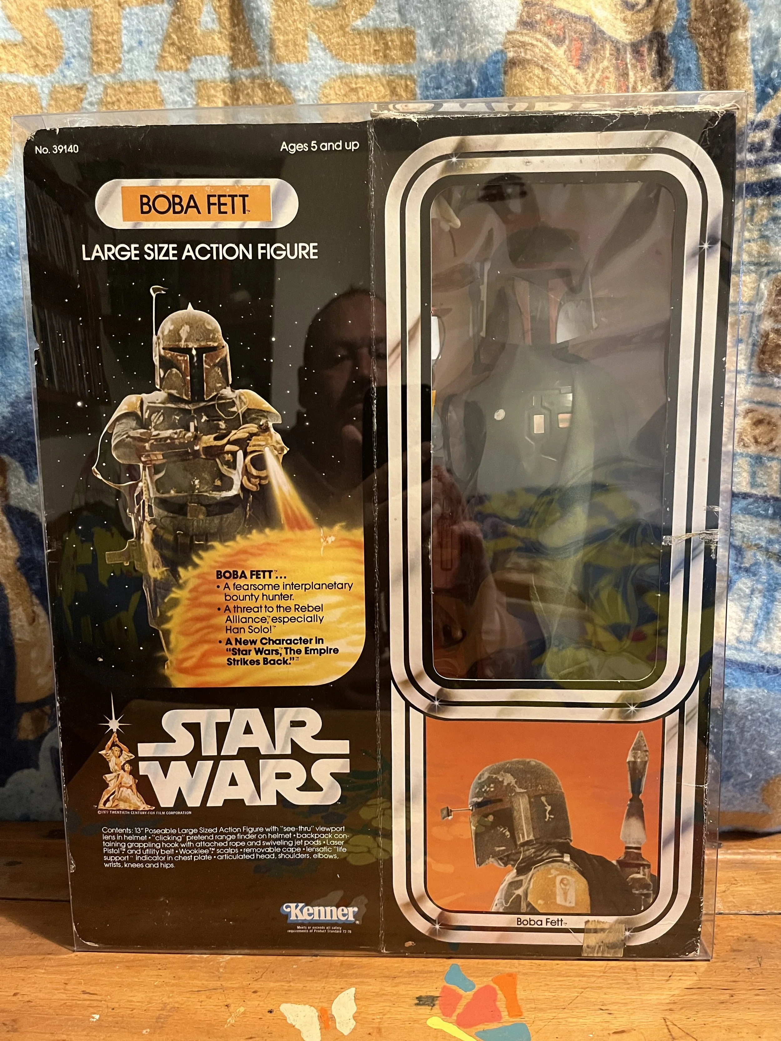 Star Wars Boba Fett action figure packaging featuring an image of Boba Fett in armor holding a flame thrower, set against a space background with stars and planets, with additional graphic elements and instruction text on the bottom.