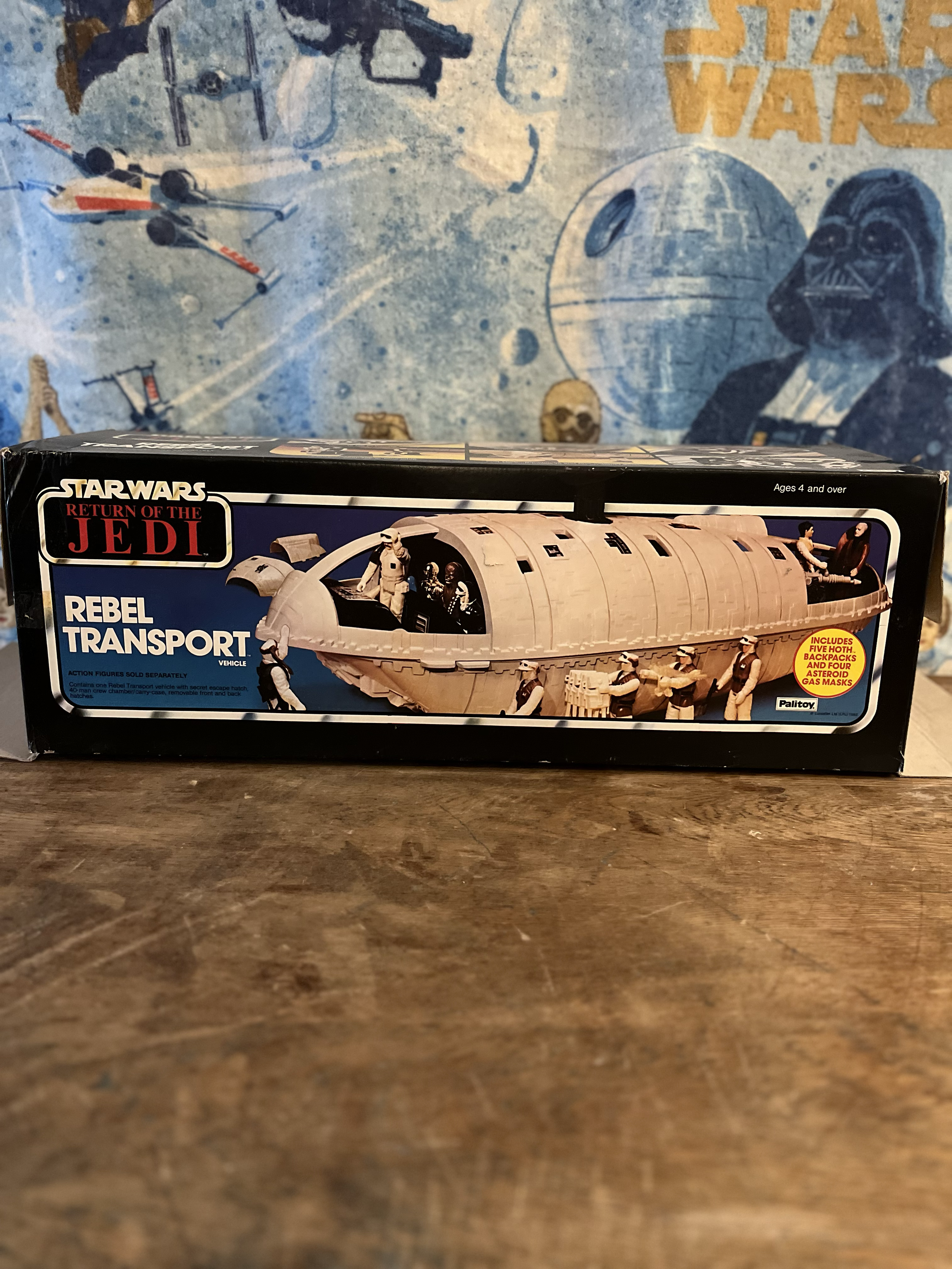 Star Wars Return of the Jedi Rebel Transport toy vehicle with action figures inside, on a wooden surface with Star Wars themed background.