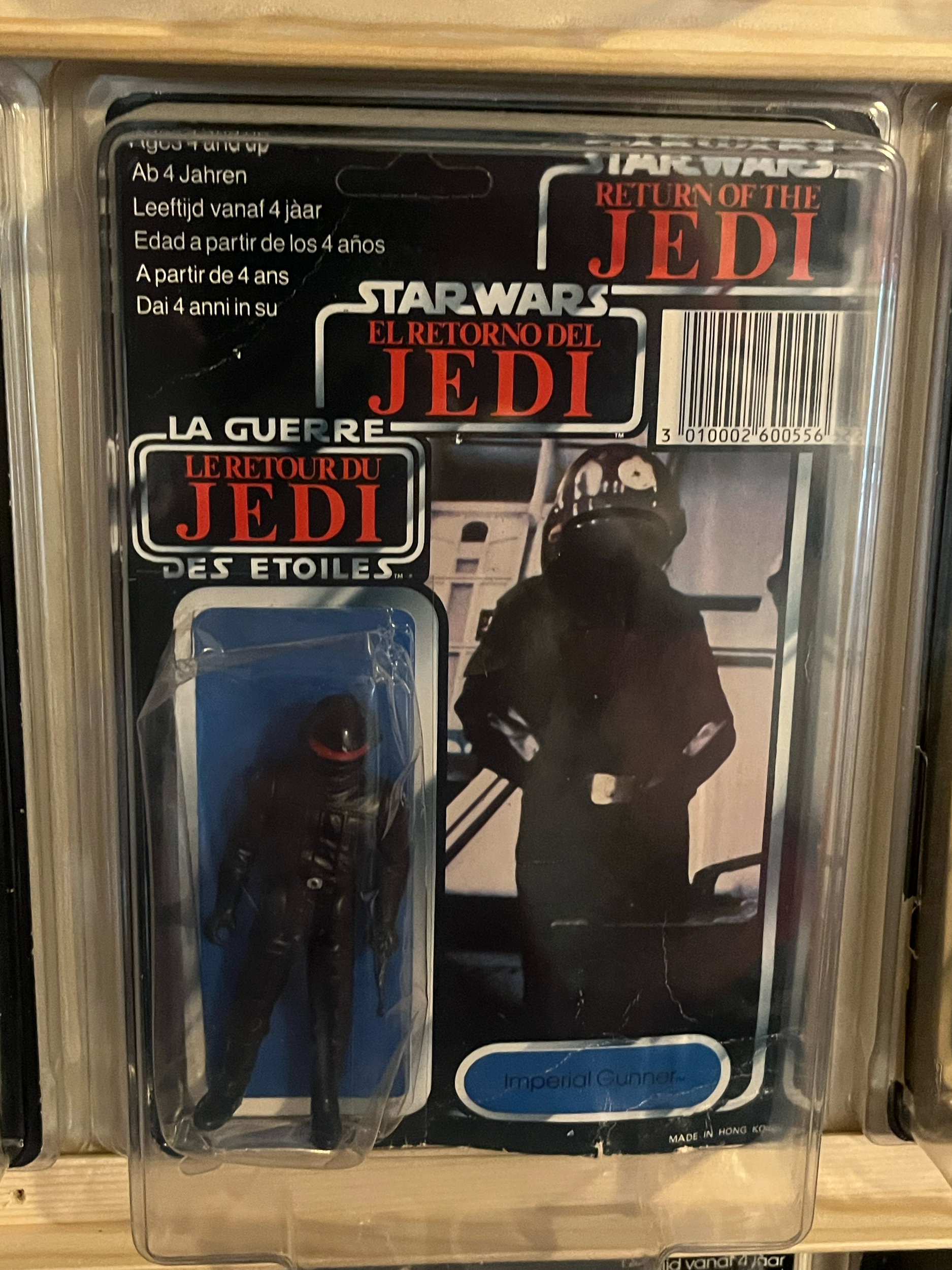 A collectible action figure toy in its packaging, depicting a black figure with some white details, possibly a fictional character from the 'Joker' series, inside a clear plastic case.
