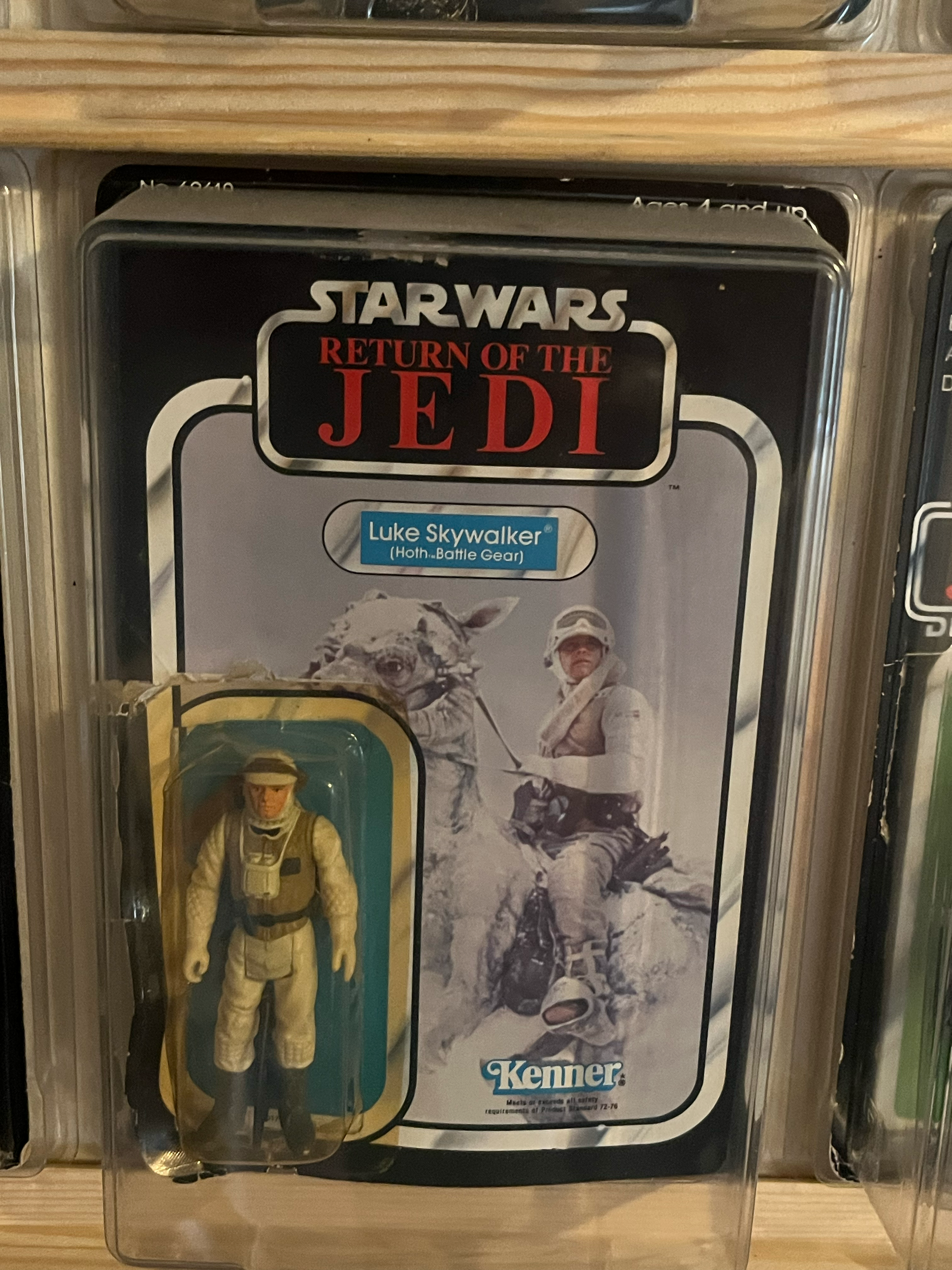 A collection of Star Wars-themed toys and memorabilia displayed in a display case. Includes a tin box with an illustration of a character in snow gear holding a weapon, and various action figures and collectibles related to Star Wars.