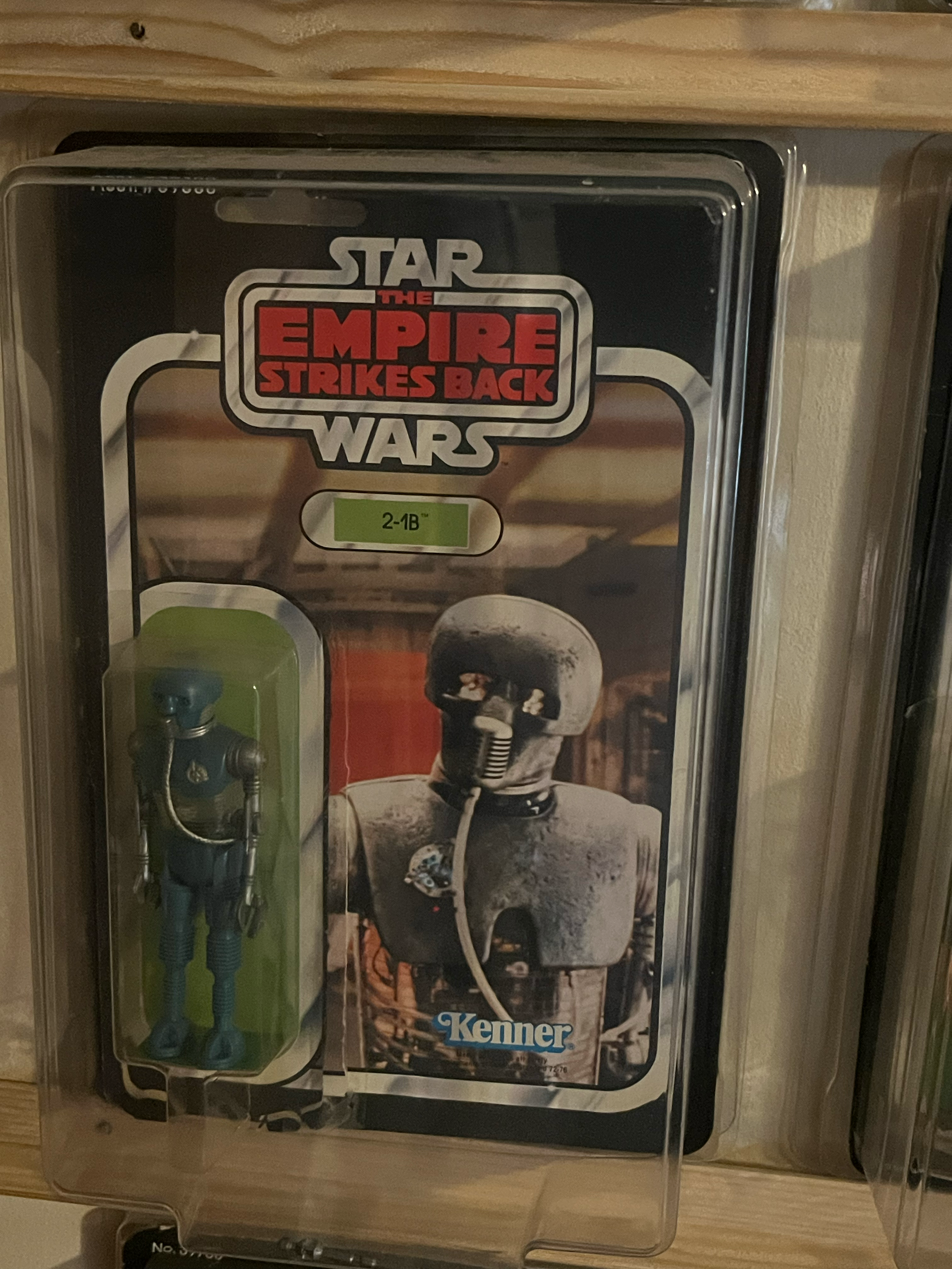 A Transformers-themed Transformer toy inside a clear plastic and cardboard packaging on a wooden shelf.