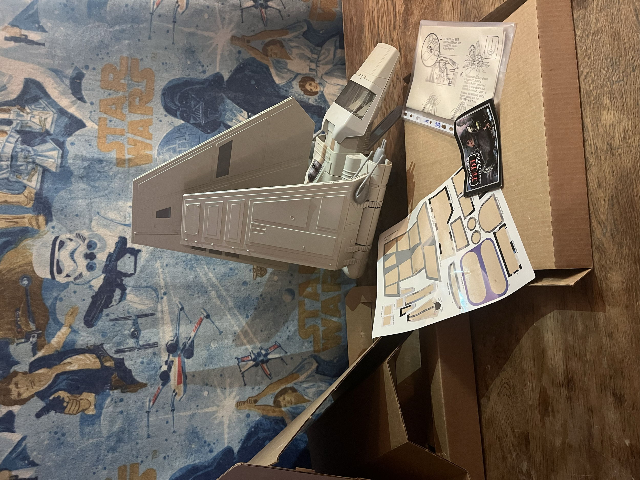 A table with various instructions, decals, and model parts for building a spaceship. There is a white plastic model spaceship, a booklet with assembly instructions, and a sticker sheet with decals visible.