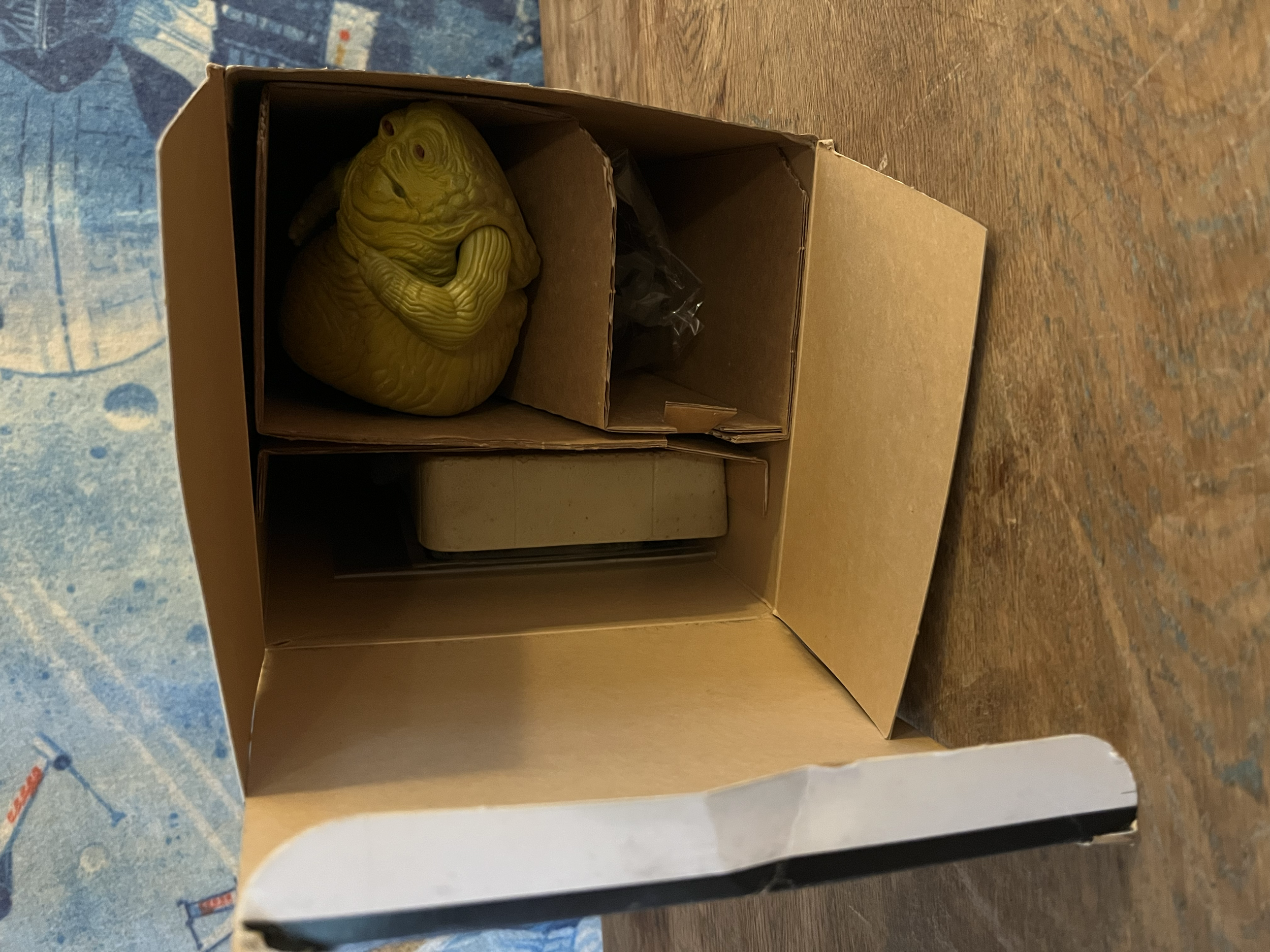 A yellow lizard figurine inside a cardboard box on a wooden surface.