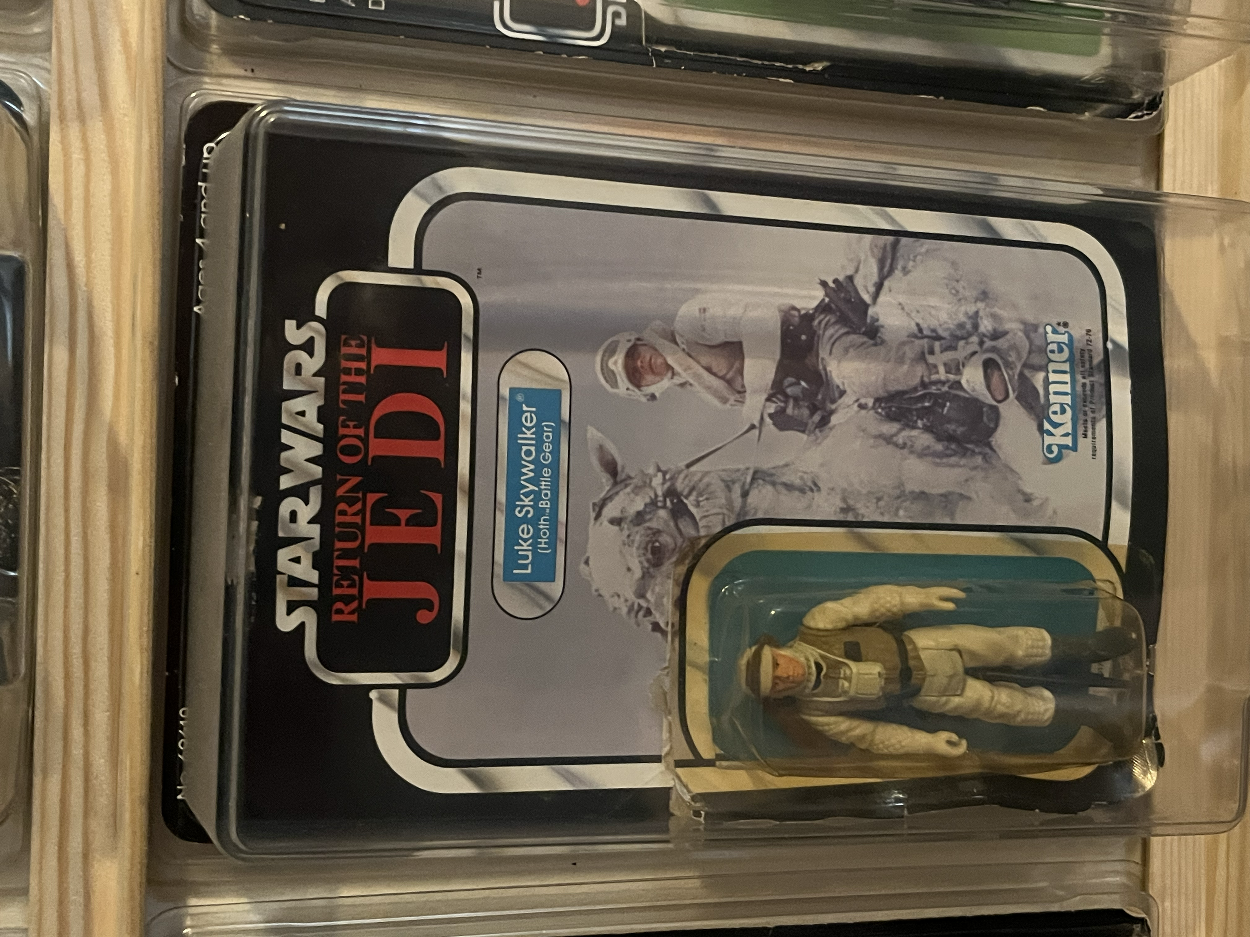 A collection of Star Wars-themed toys and memorabilia displayed in a display case. Includes a tin box with an illustration of a character in snow gear holding a weapon, and various action figures and collectibles related to Star Wars.