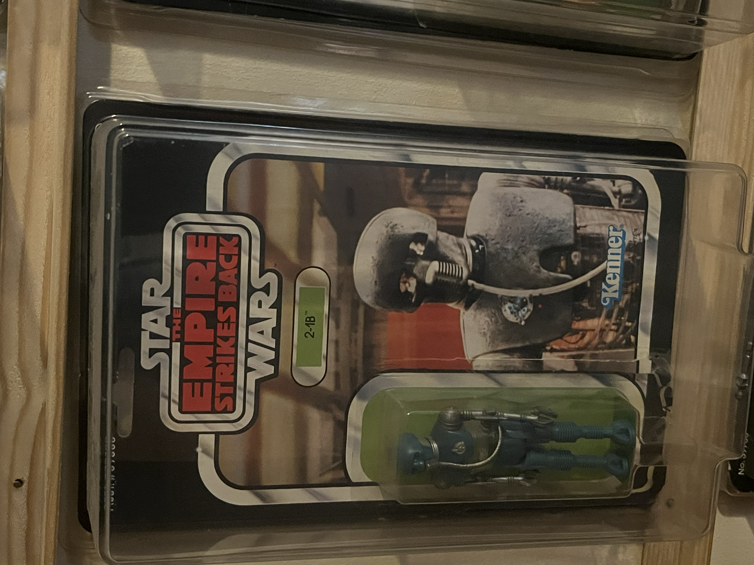 A Transformers-themed Transformer toy inside a clear plastic and cardboard packaging on a wooden shelf.