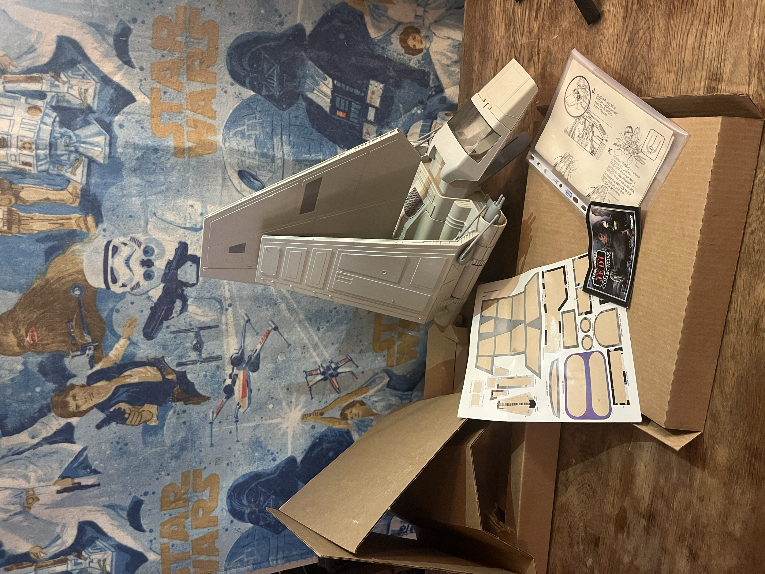 Star Wars themed display with manuals, models, and packages on a wooden table against a Star Wars mural.
