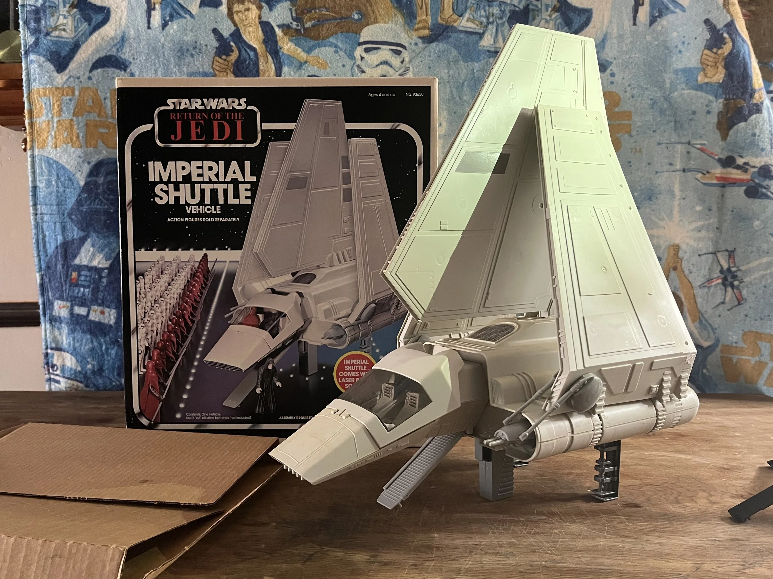 Star Wars Return of the Jedi Imperial Shuttle building toy with a cardboard box and the assembled model on a wooden surface, with a Star Wars themed cloth in the background.