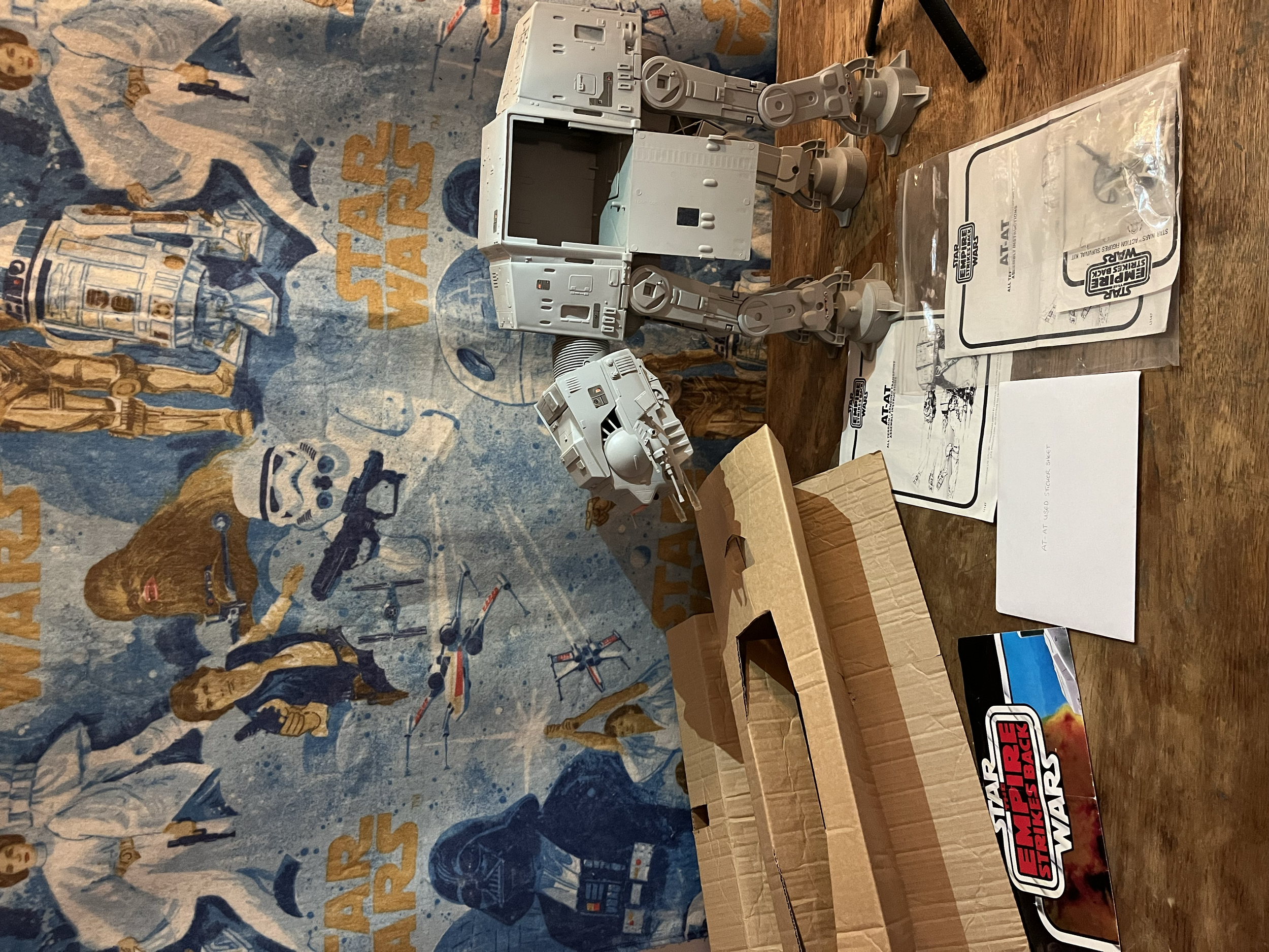 Various Star Wars themed toy parts and packaging on a wooden surface with a Star Wars poster or tapestry in the background.