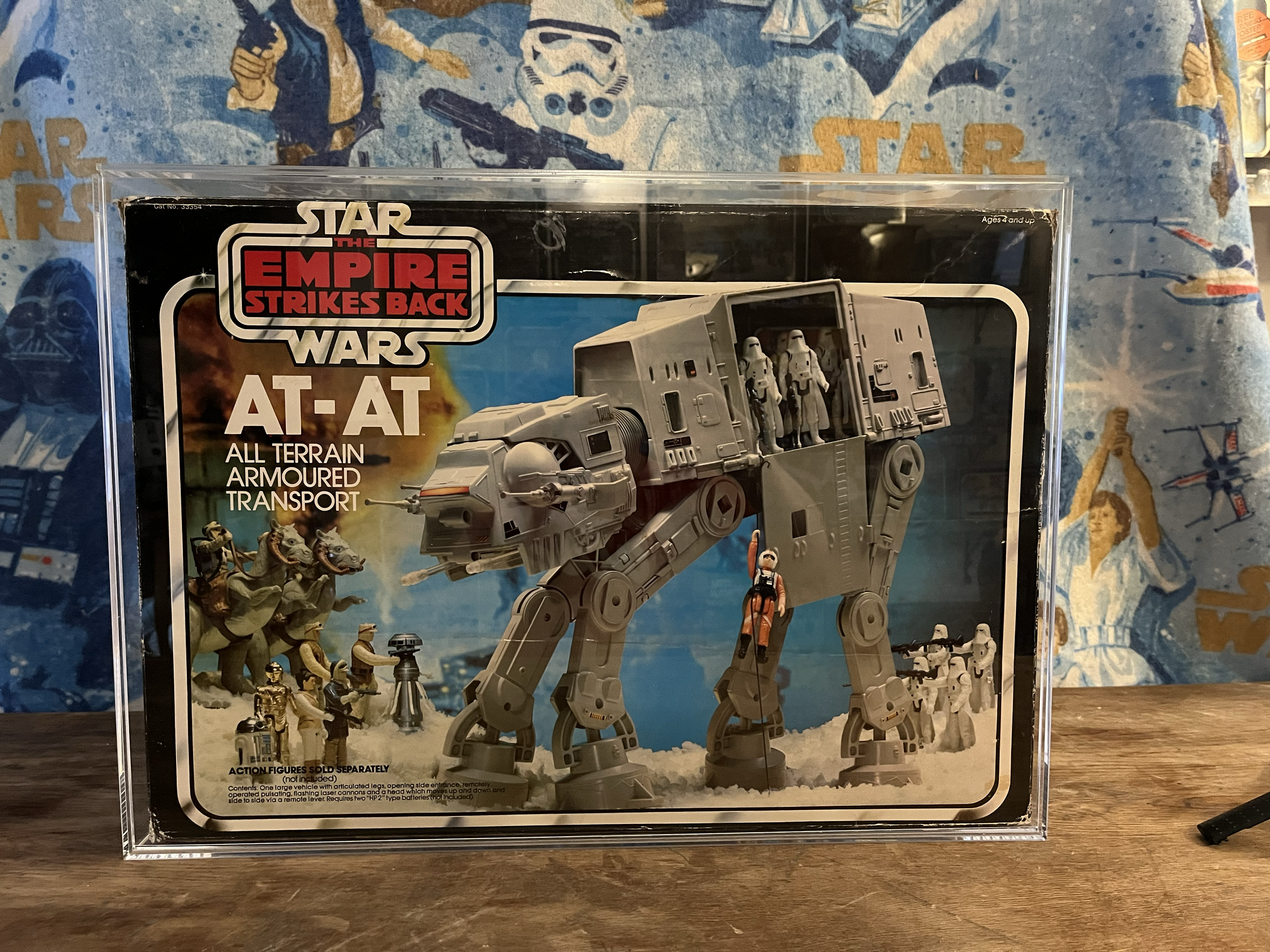 Star Wars action figure set in clear display case featuring a large AT-AT walker, smaller vehicles, and multiple Stormtrooper figures, with a blue Star Wars-themed background.