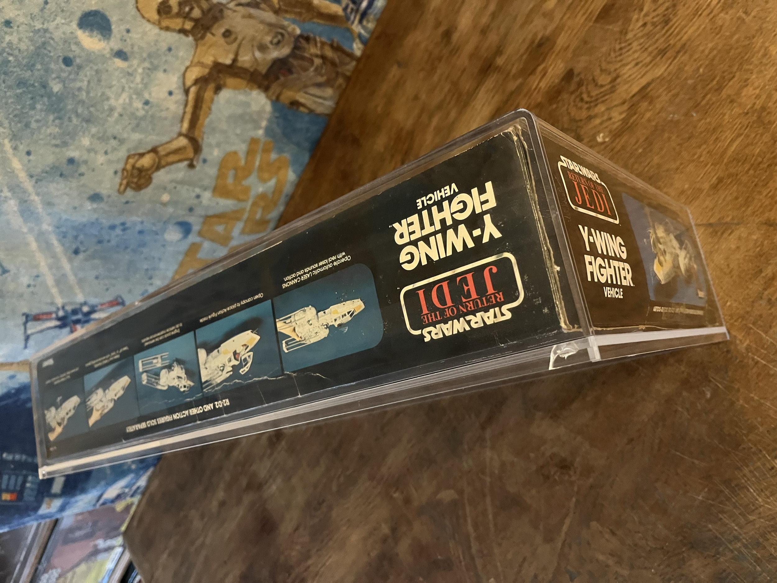 A vintage Star Wars Kenner Y-Wing Fighter boxed featuring artwork of the spacecraft, placed on a wooden surface with another Star Wars model kit box visible in the background.