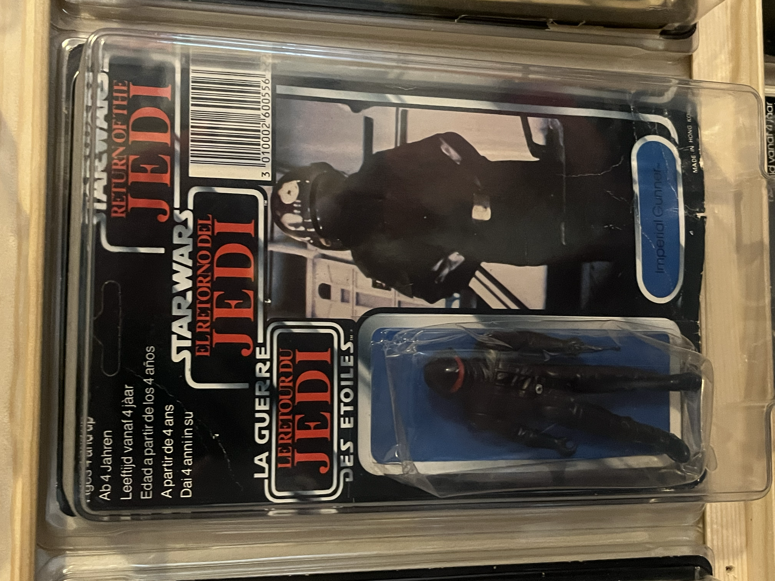 A collectible action figure toy in its packaging, depicting a black figure with some white details, possibly a fictional character from the 'Joker' series, inside a clear plastic case.